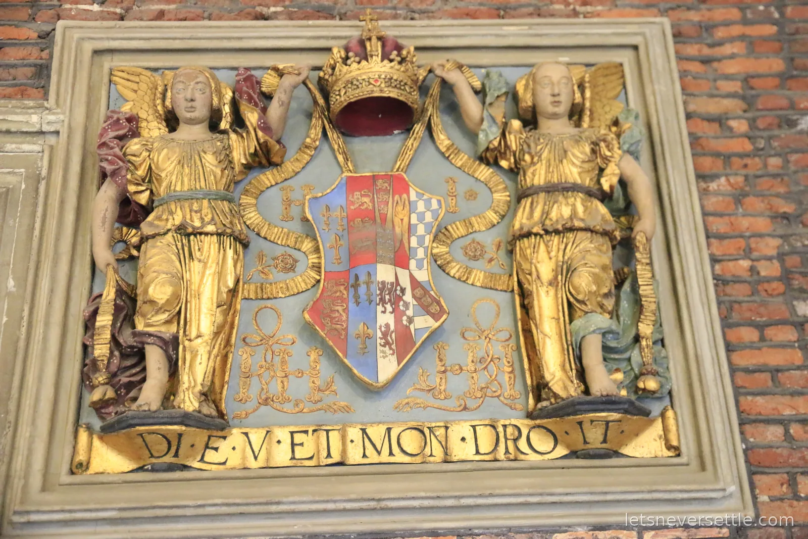 A painted royal coat of arms at Hampton Court Palace with angels above a scroll reading Dieu et mon droit