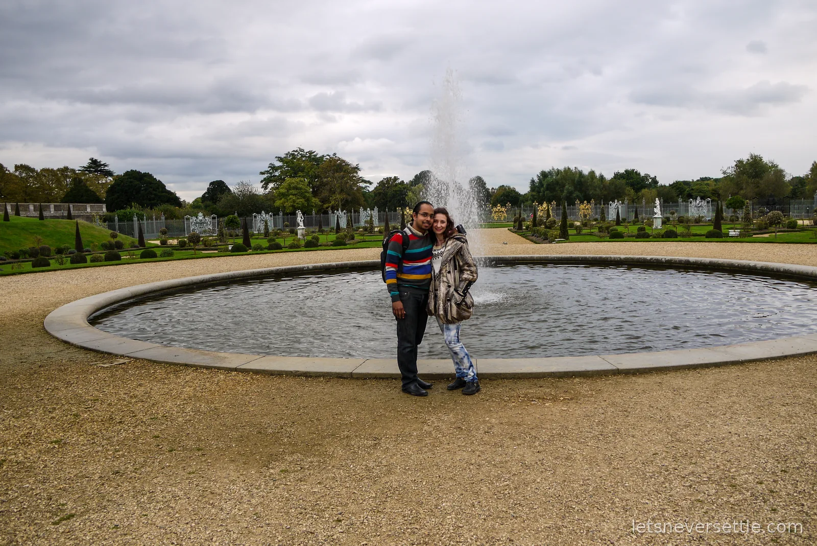 Inga and Dileep standing in front of a round fountain pool in the Great Fountain Garden at Hampton Court Palace