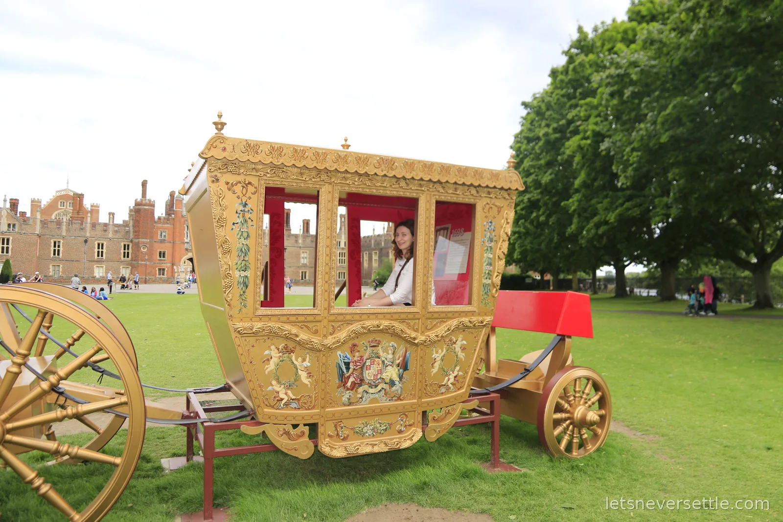 Inga sitting in a golden carriage prop in front of the turreted Tudor west front of Hampton Court Palace