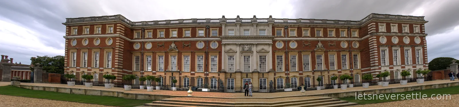 Stitched panorama of the long baroque south front of Hampton Court Palace with potted trees along the terrace