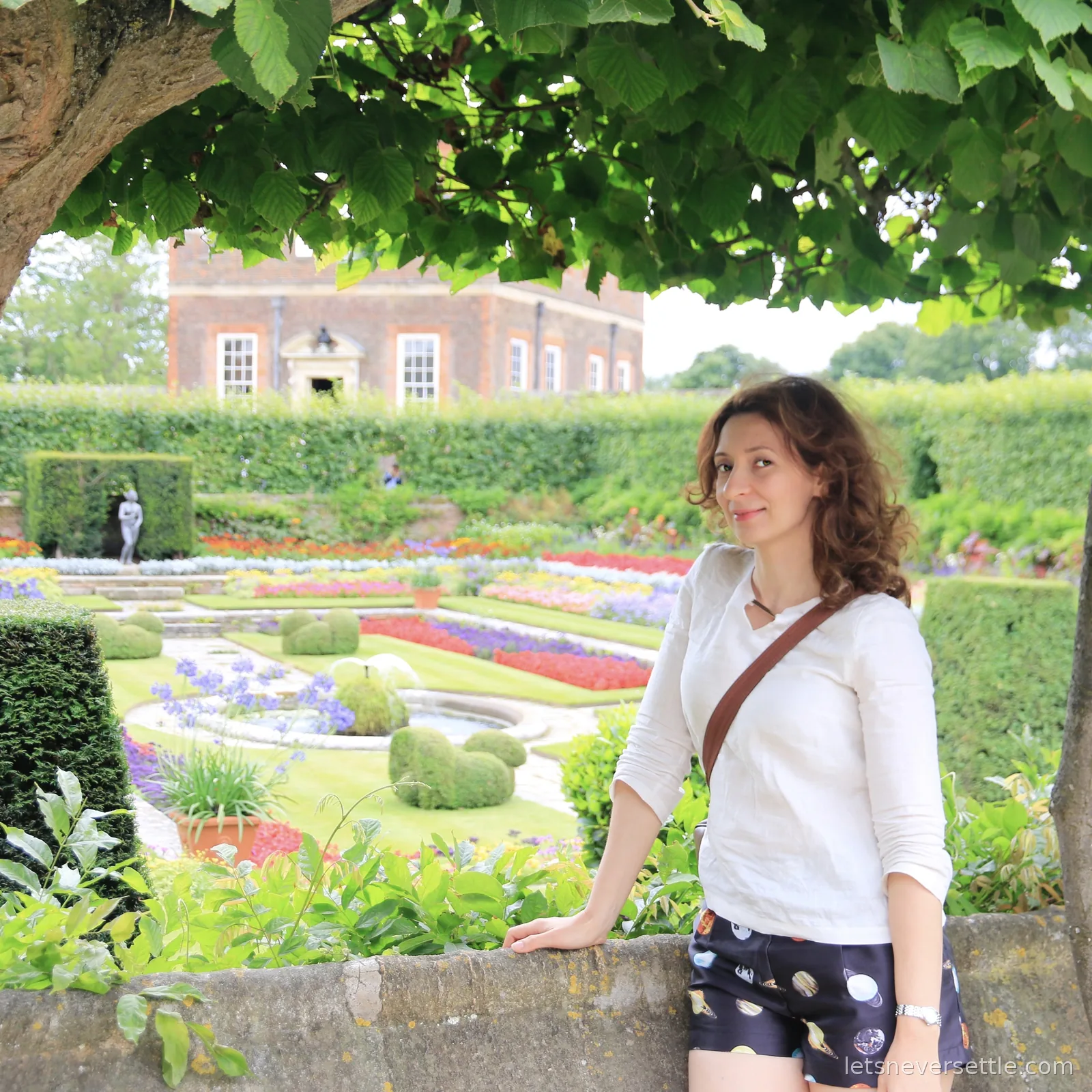 Inga leaning on the stone balustrade above the sunken garden at Hampton Court, with beds of purple and red planting and clipped topiary cones below
