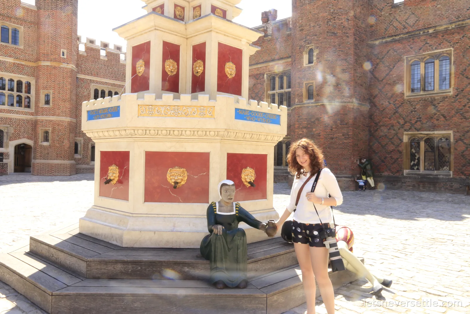 Inga beside the golden wine fountain in the Tudor brick Base Court of Hampton Court Palace, costumed figures nearby