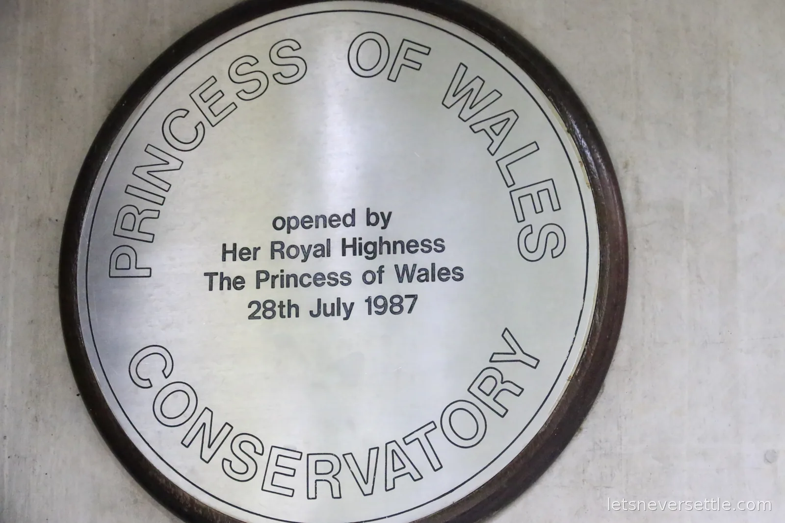 A round metal plaque reading Princess of Wales Conservatory, opened by Her Royal Highness The Princess of Wales, 28th July 1987