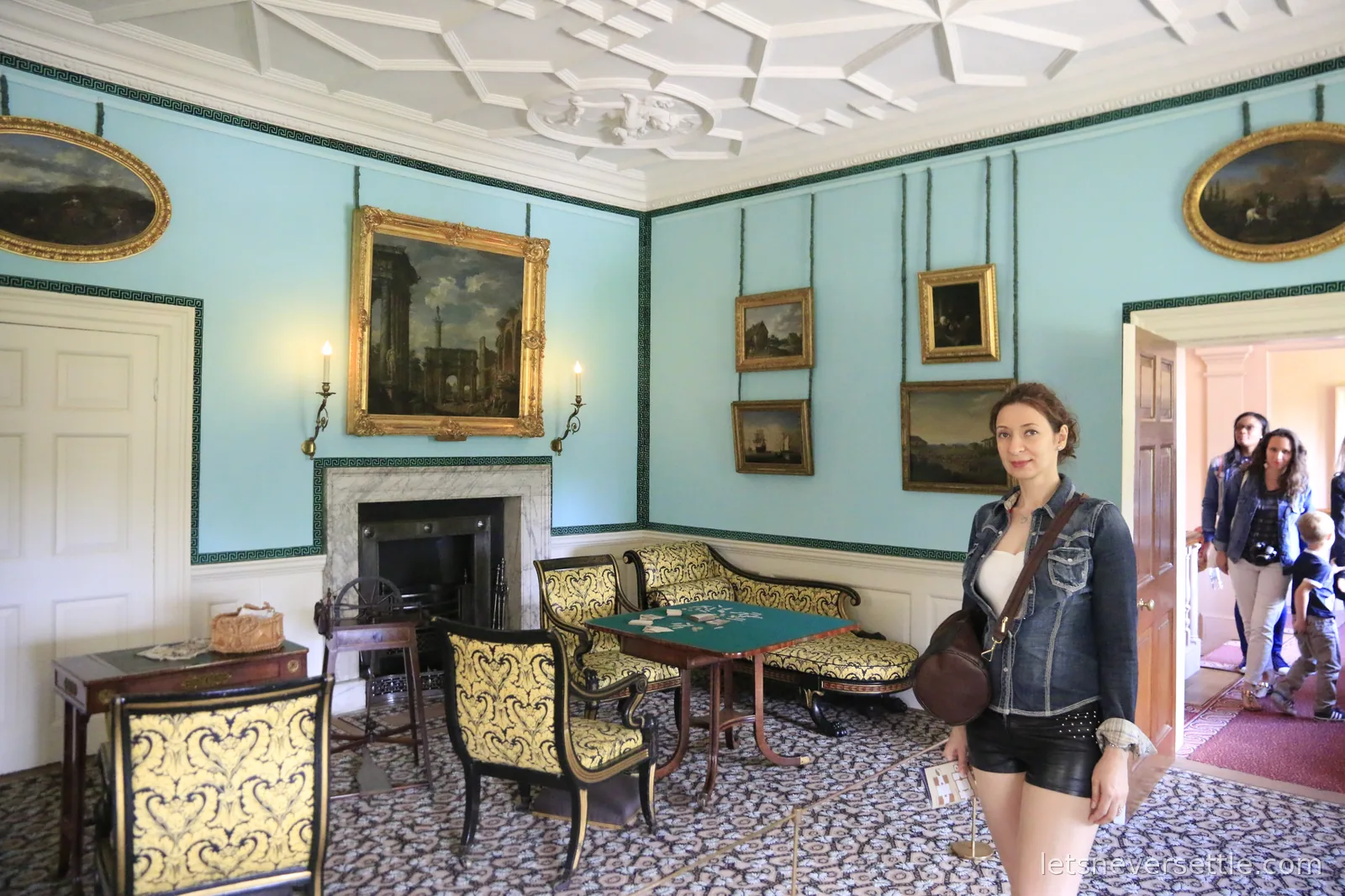 Inga standing in a Georgian drawing room in Kew Palace with powder blue walls, a card table and gilt framed portraits