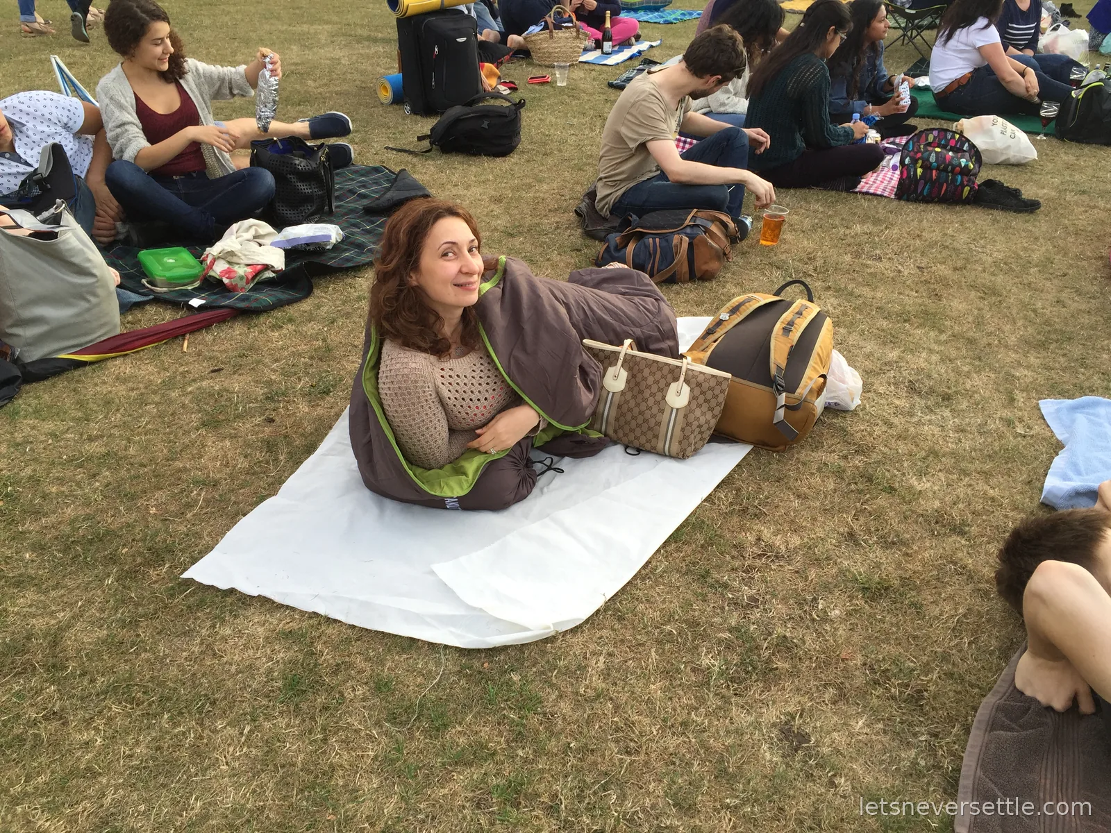 Inga wrapped in a blanket on a picnic rug on the grass at Kew among other film-goers with their bags, bottles and food