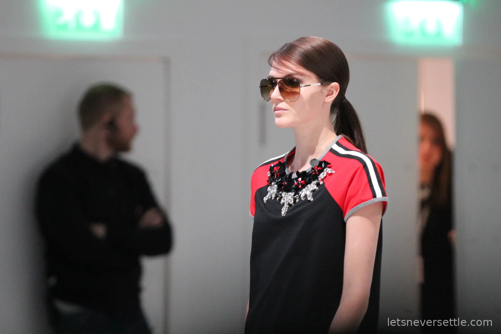 Close-up of a model in aviator sunglasses wearing a black and red raglan tee with a large crystal and flower necklace