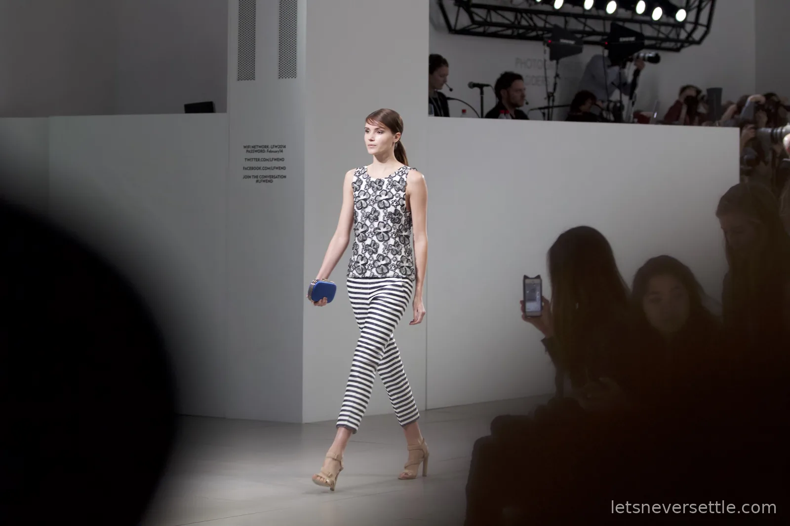A model in a monochrome lace top and striped cropped trousers carrying a small blue clutch on the catwalk