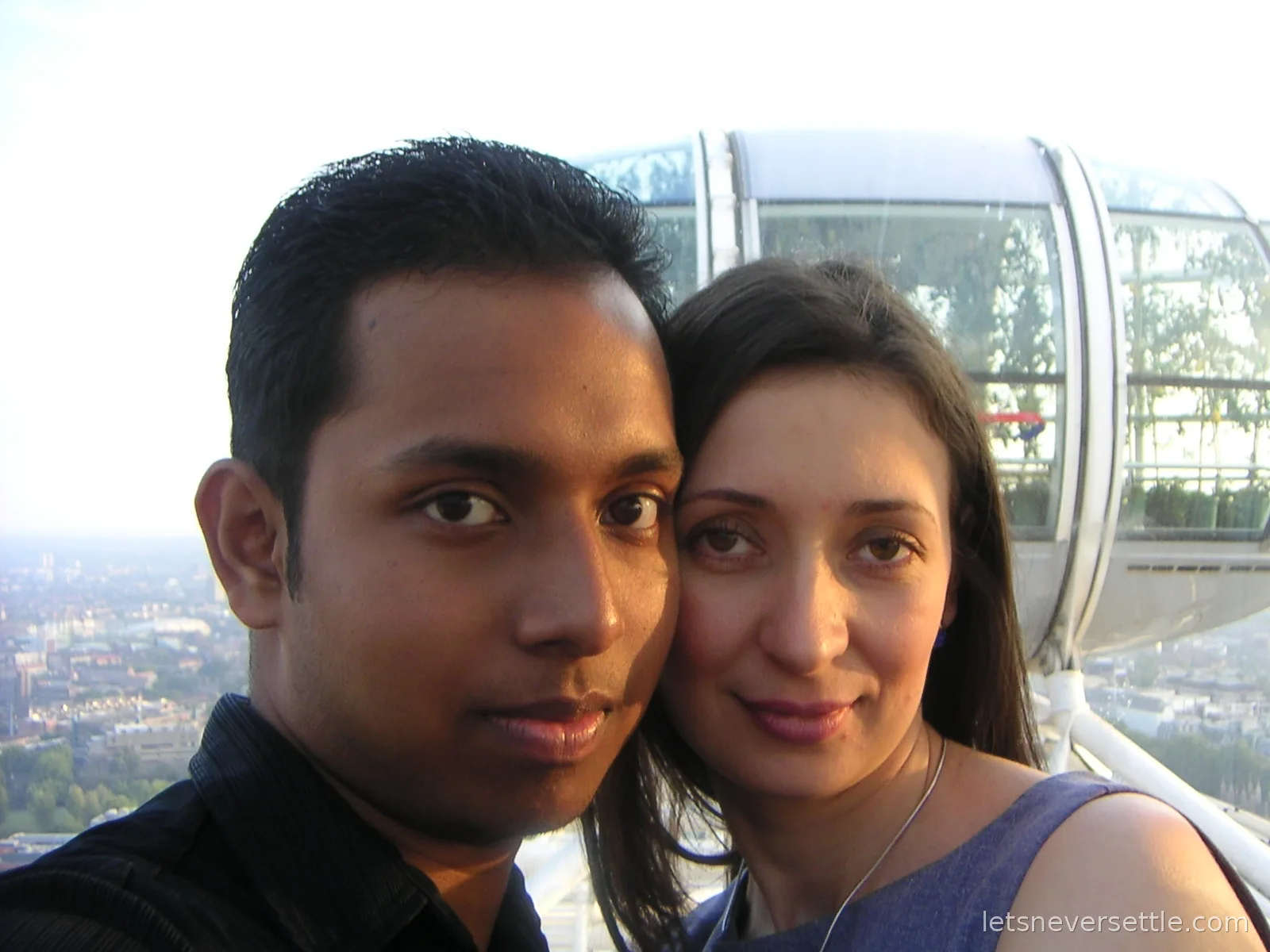 Close selfie of Dileep and Inga cheek to cheek high on the London Eye, a glass capsule and the city stretching away below behind them