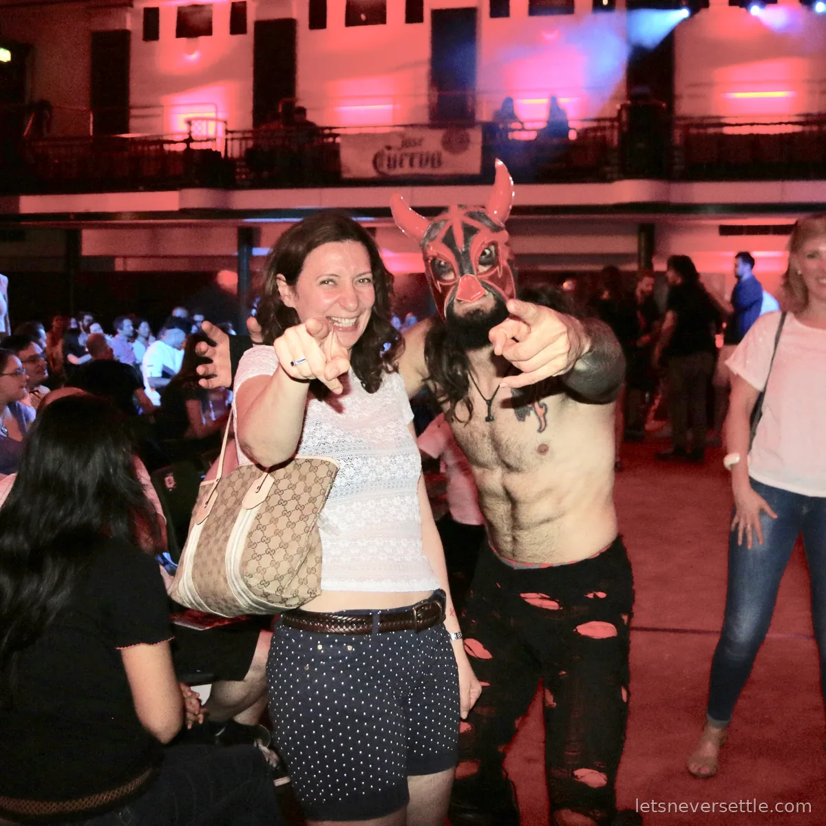 Inga pointing at the camera in the crowd at York Hall beside a masked wrestler in torn black trousers striking the same pose