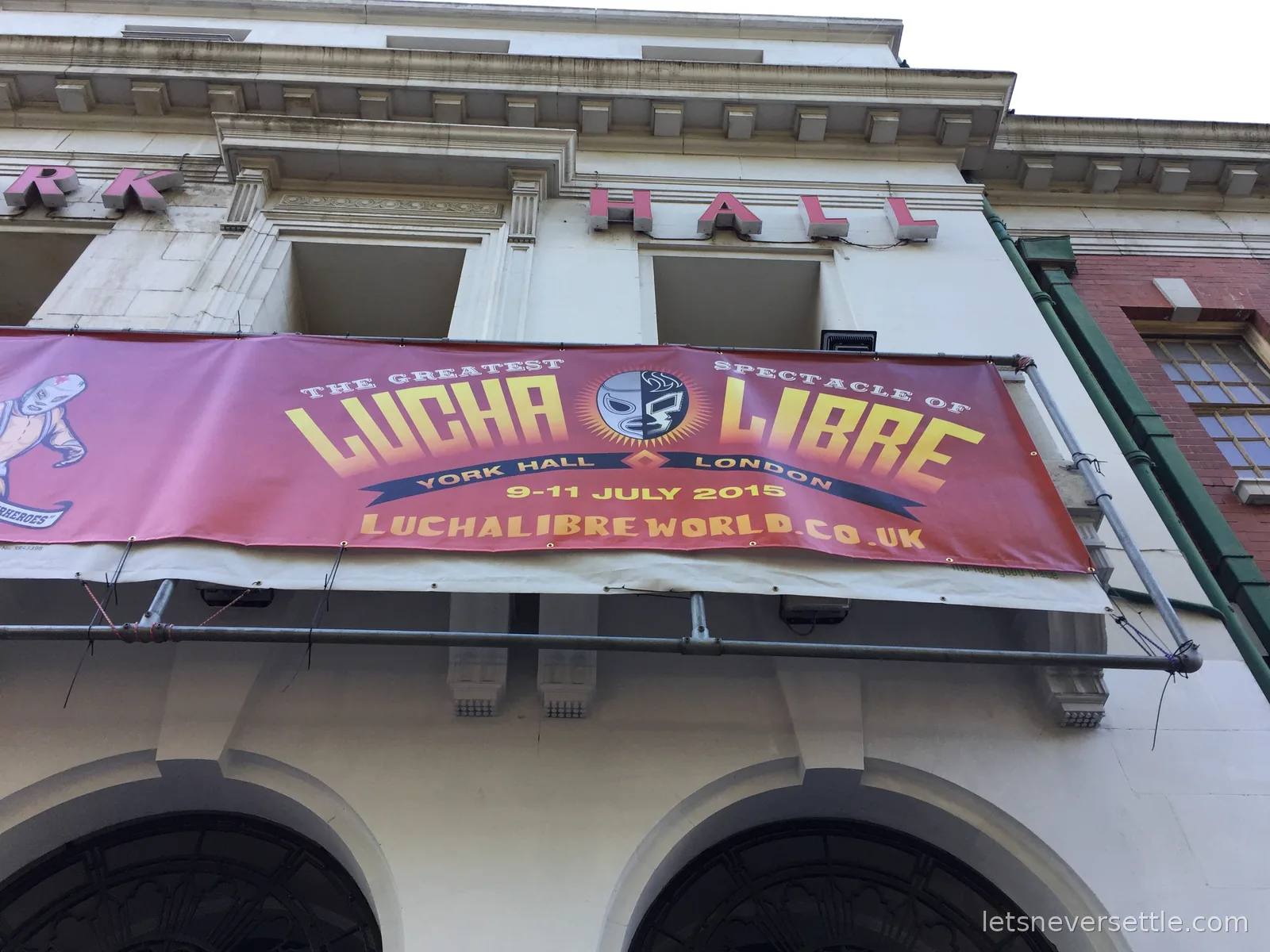 A banner reading The Greatest Spectacle of Lucha Libre, York Hall London, 9 to 11 July 2015, strung across the stone front of York Hall
