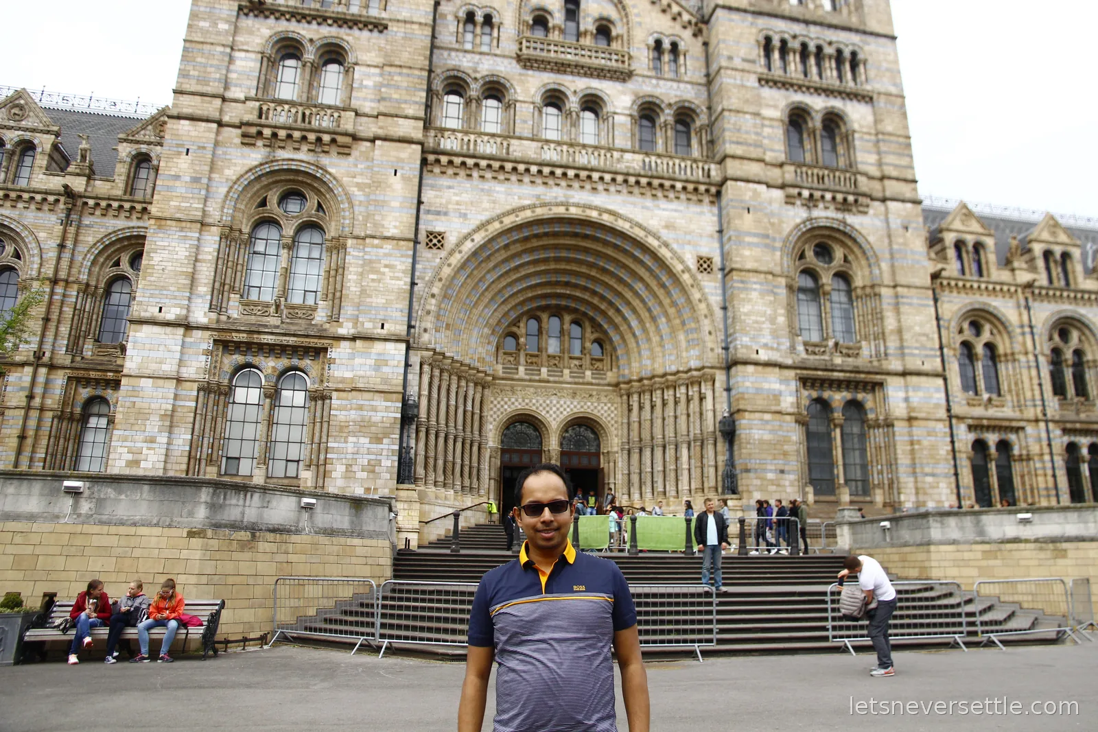 Dileep standing at the foot of the steps in front of the Romanesque terracotta facade of the Natural History Museum