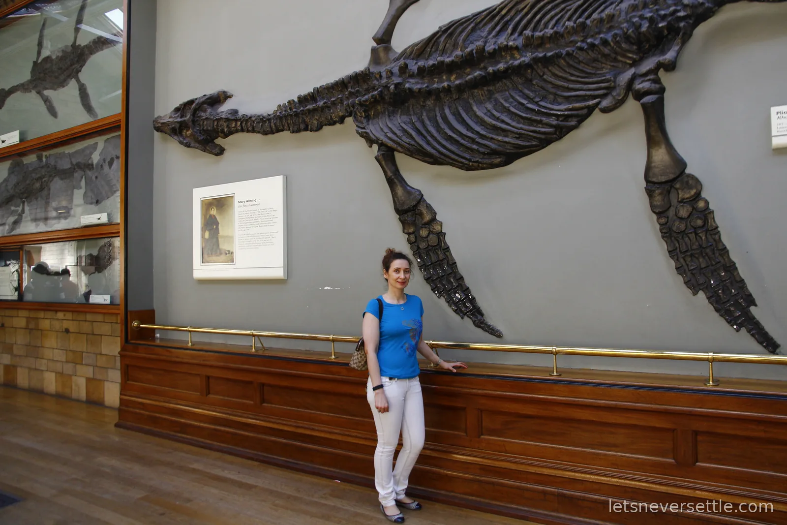 Inga standing beneath a large fossilised marine reptile skeleton mounted on the gallery wall, its long flippers spread wide