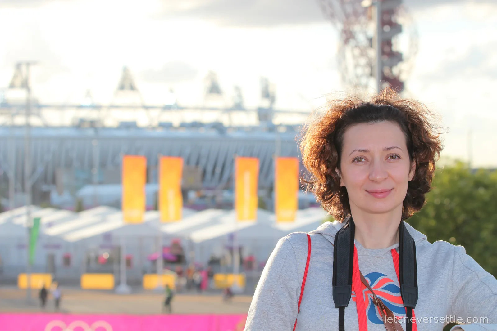 Inga with a Team GB lanyard in the Olympic Park, the Olympic Stadium and orange banners soft in the background