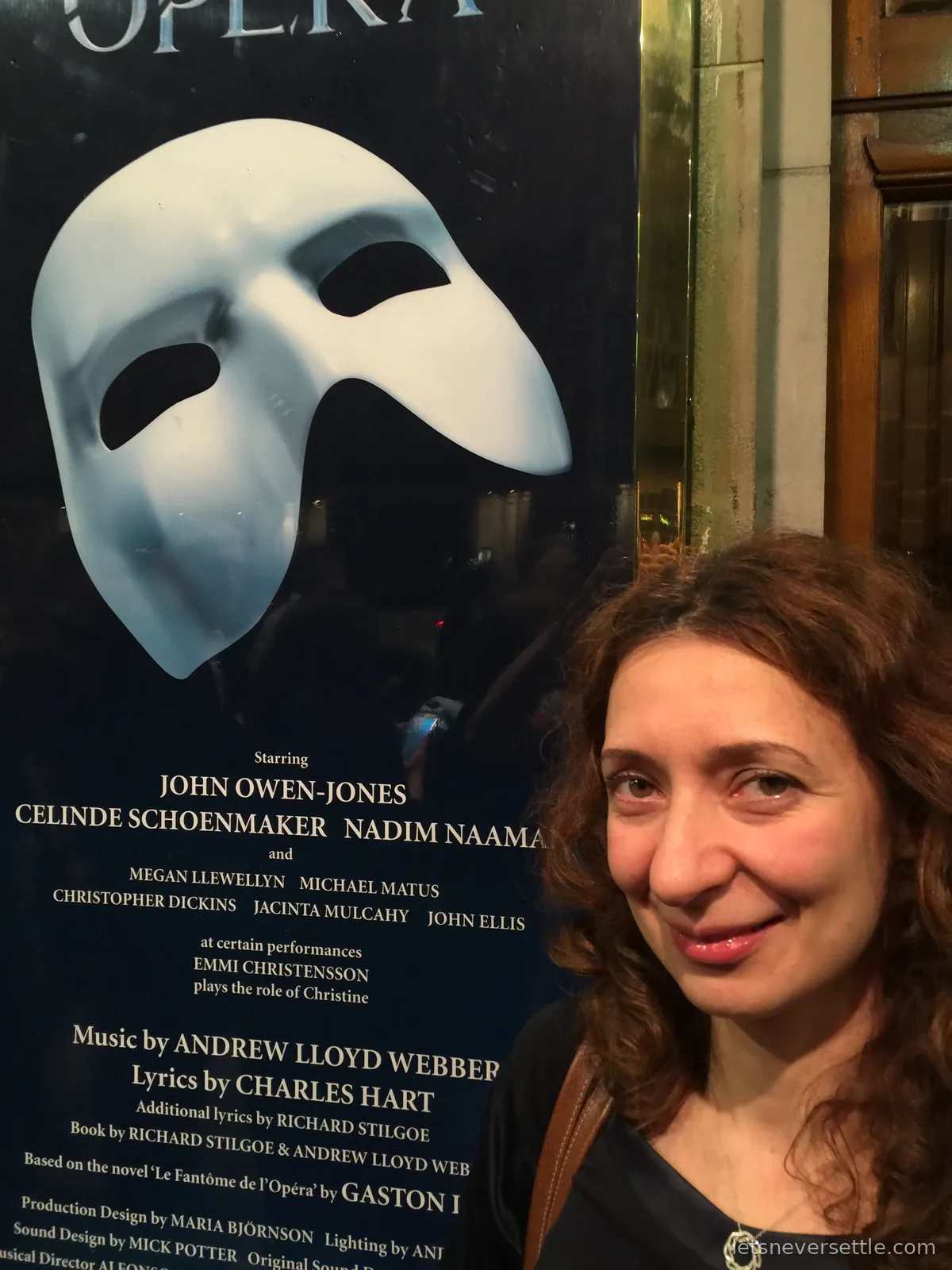 Inga beside the Phantom of the Opera poster with its white mask outside the theatre at night