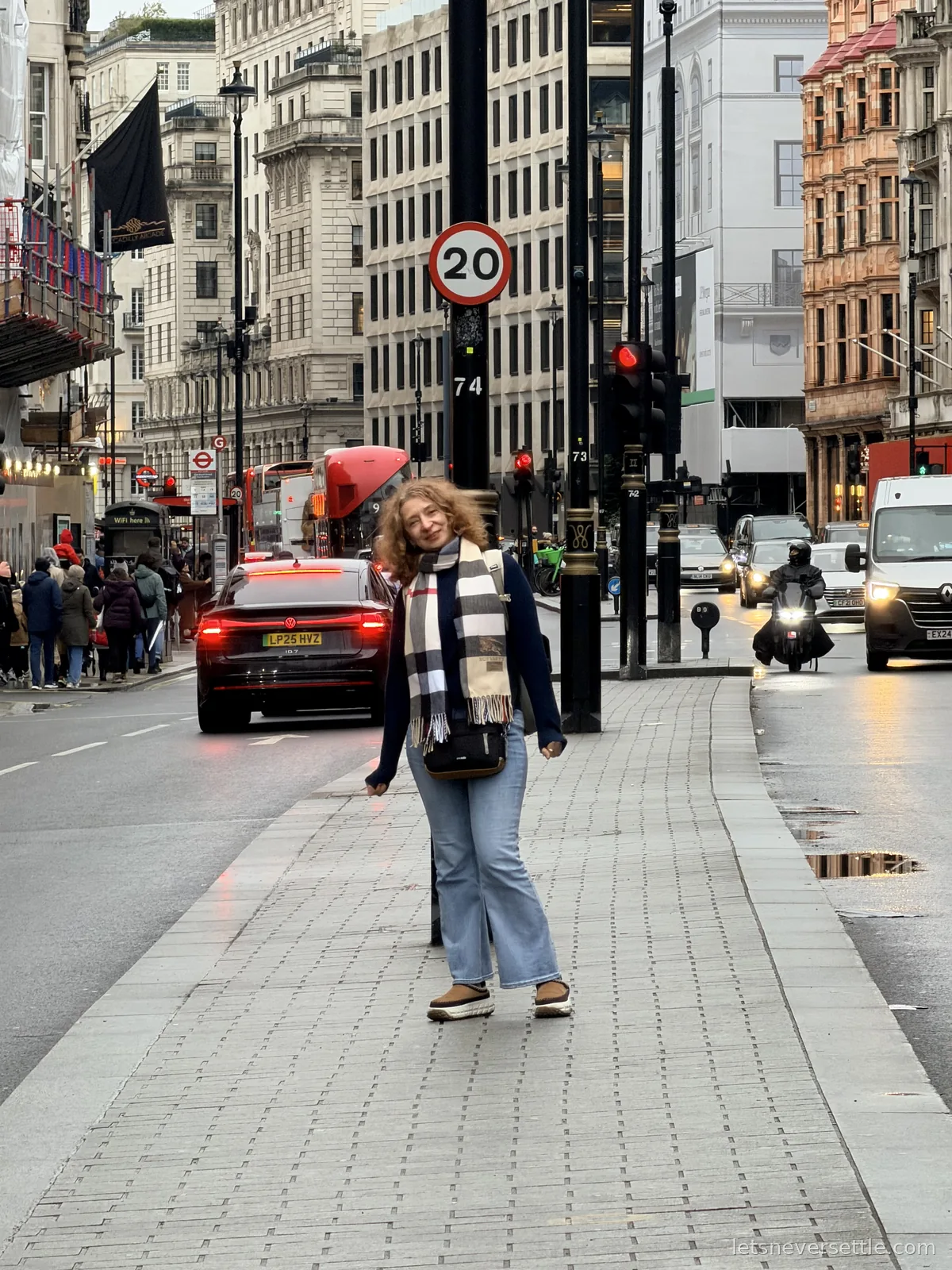 Inga in a check scarf crossing a wide street near Piccadilly Circus with red buses, taxis and a 20 mph sign behind