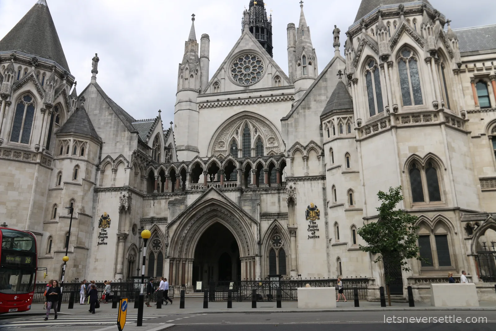 The Gothic stone frontage and spires of the Royal Courts of Justice on the Strand under a grey sky, a red bus passing on the left