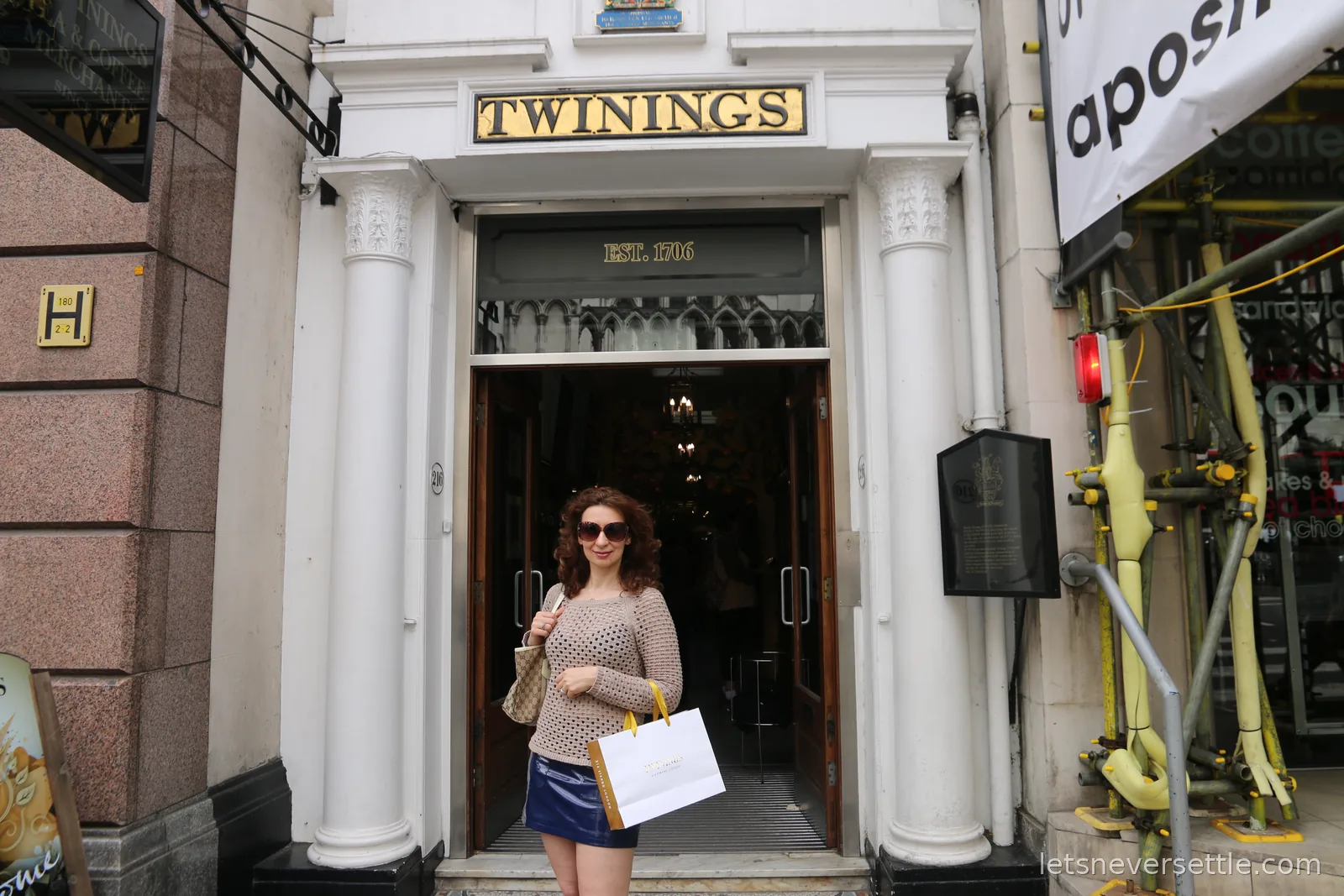 Inga in sunglasses stepping out of the Twinings doorway on the Strand carrying a paper shopping bag