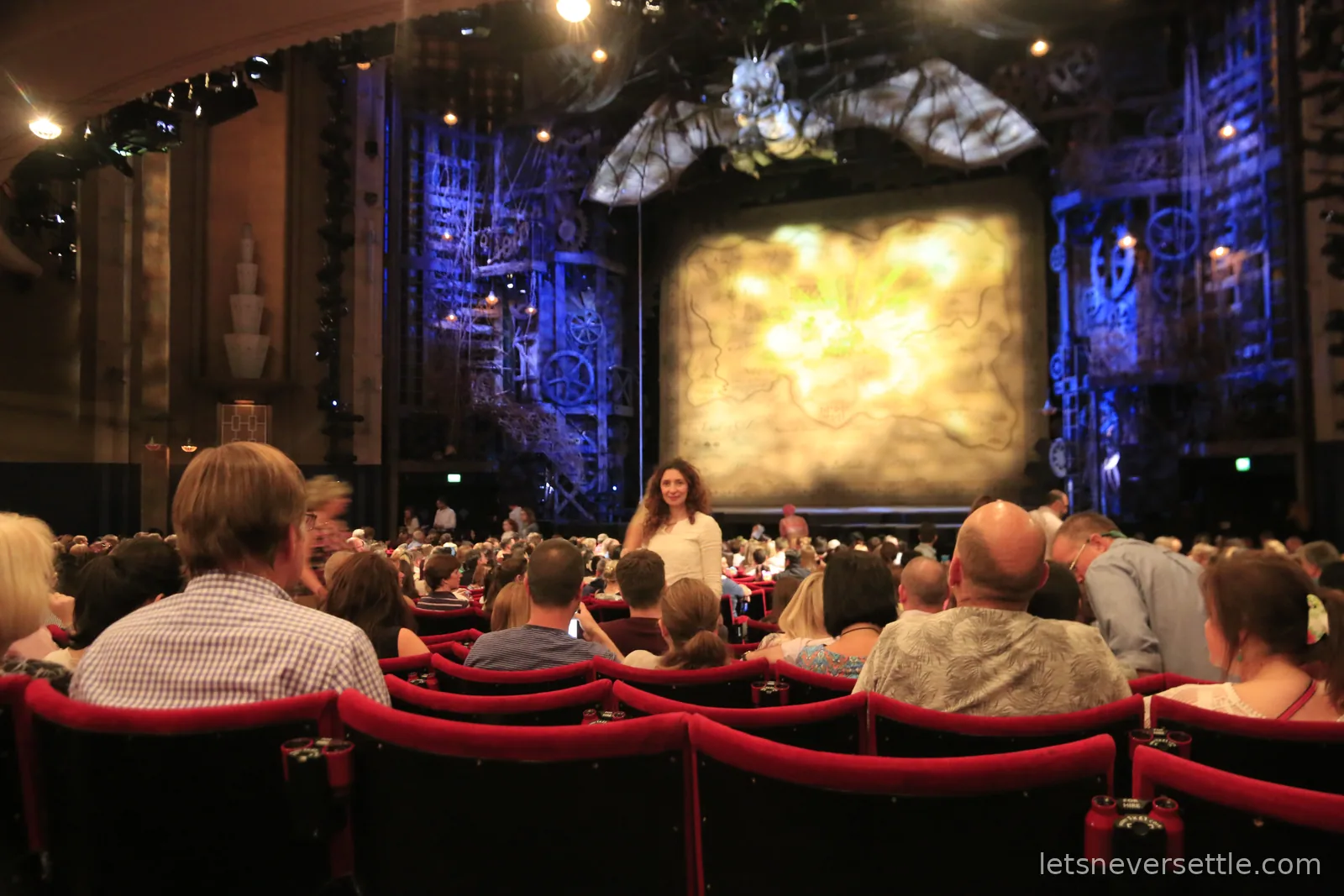 The stage before Wicked begins, a huge mechanical dragon mounted above the proscenium arch and a golden map of Oz across the curtain, the auditorium filling below
