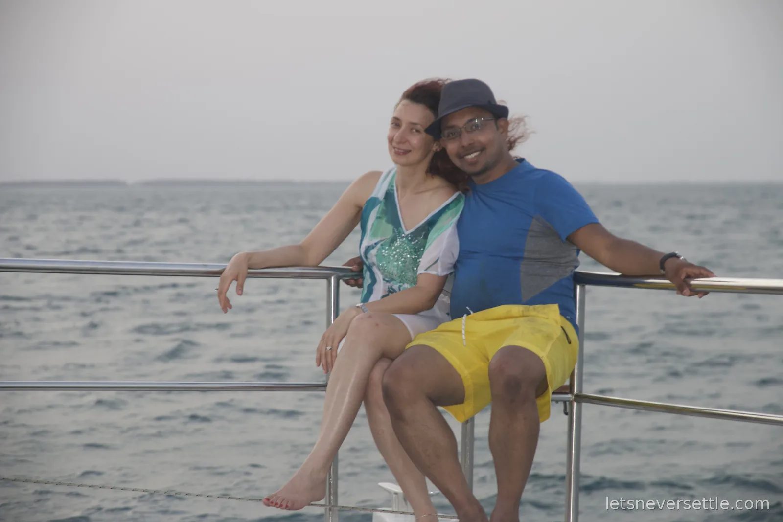 Inga and Dileep sitting together on the rail of a catamaran with the open sea behind them
