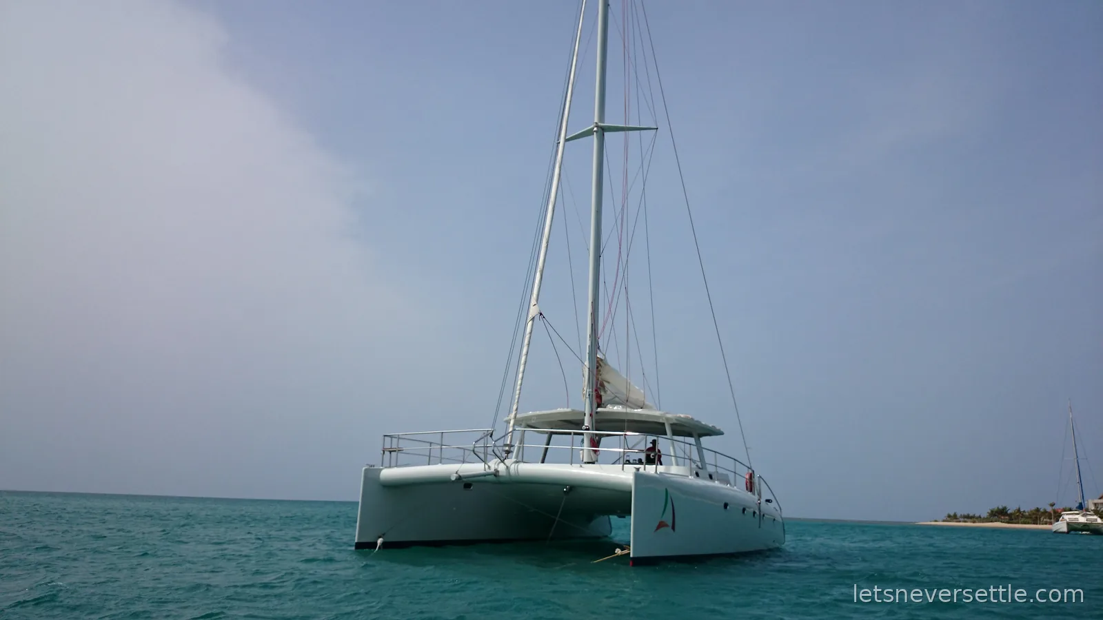 A white sailing catamaran anchored on turquoise water off the palm-lined Pasikuda shore