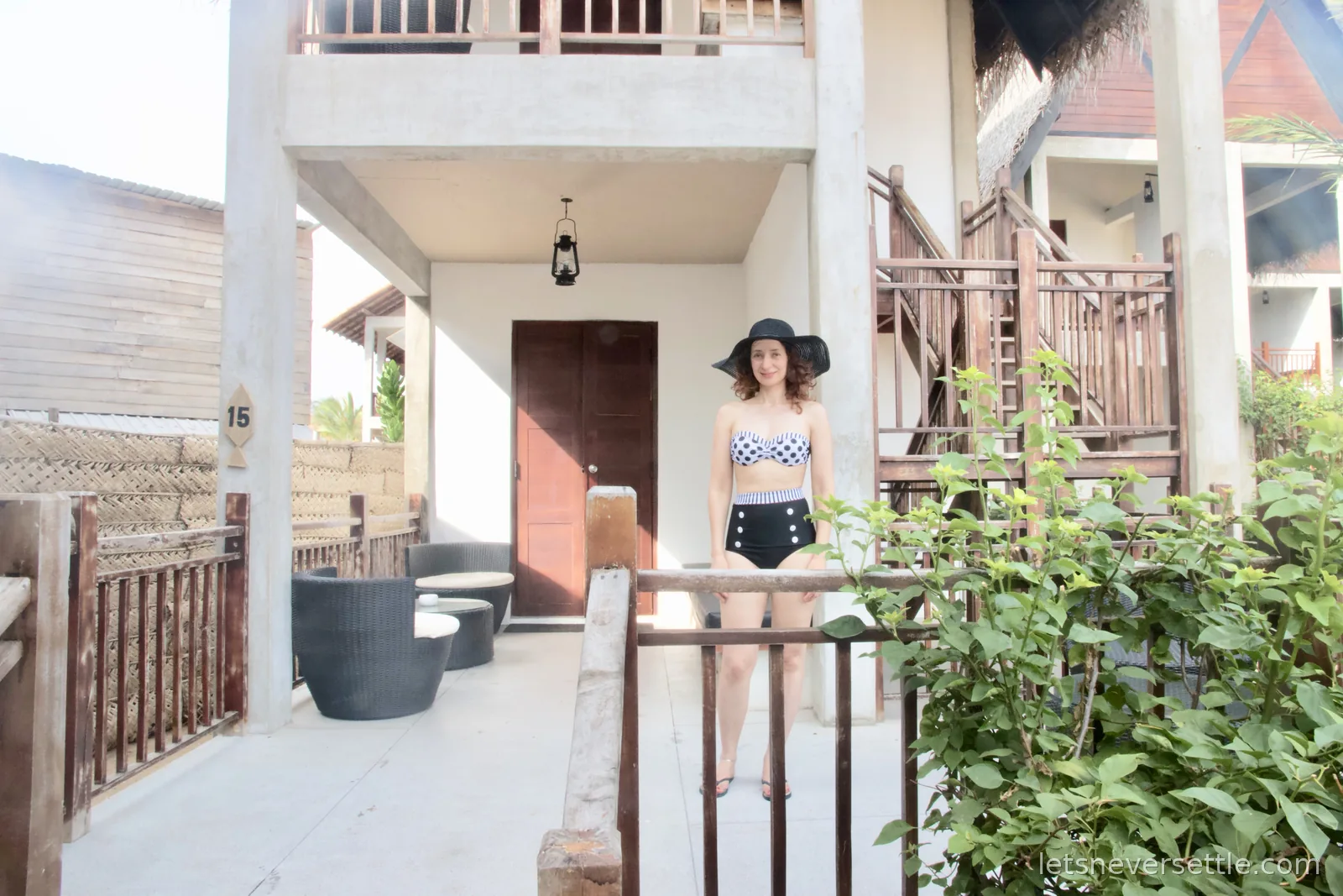 Inga in a black sun hat and polka-dot swimsuit standing on the terrace of timber chalet number 15