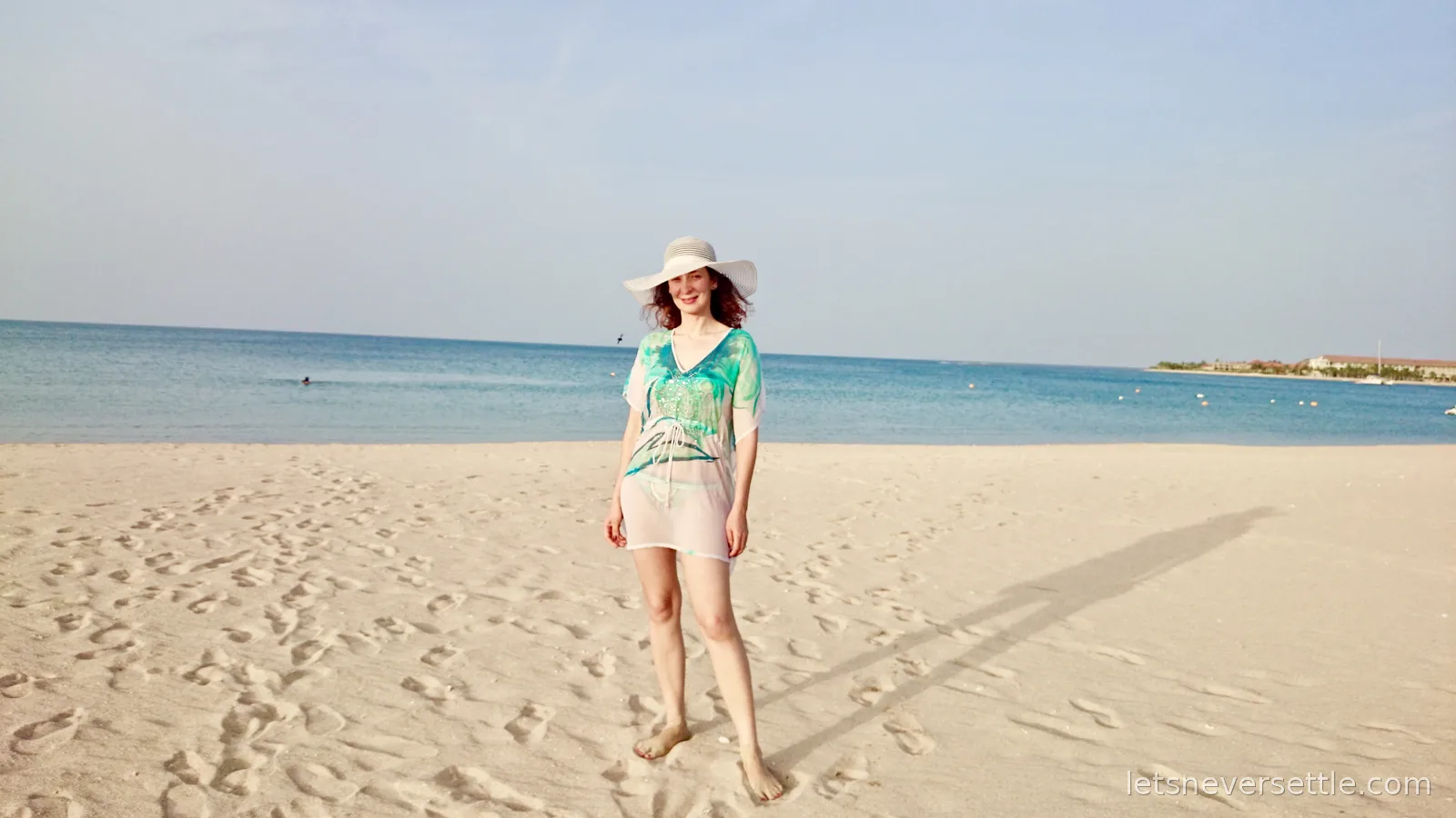 Inga in a white sun hat and sheer beach dress standing barefoot on the wide sand of Pasikuda beach