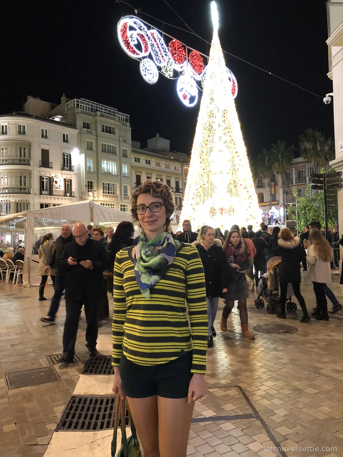 A giant cone of golden Christmas lights towering over a crowded pedestrian street in Malaga at night