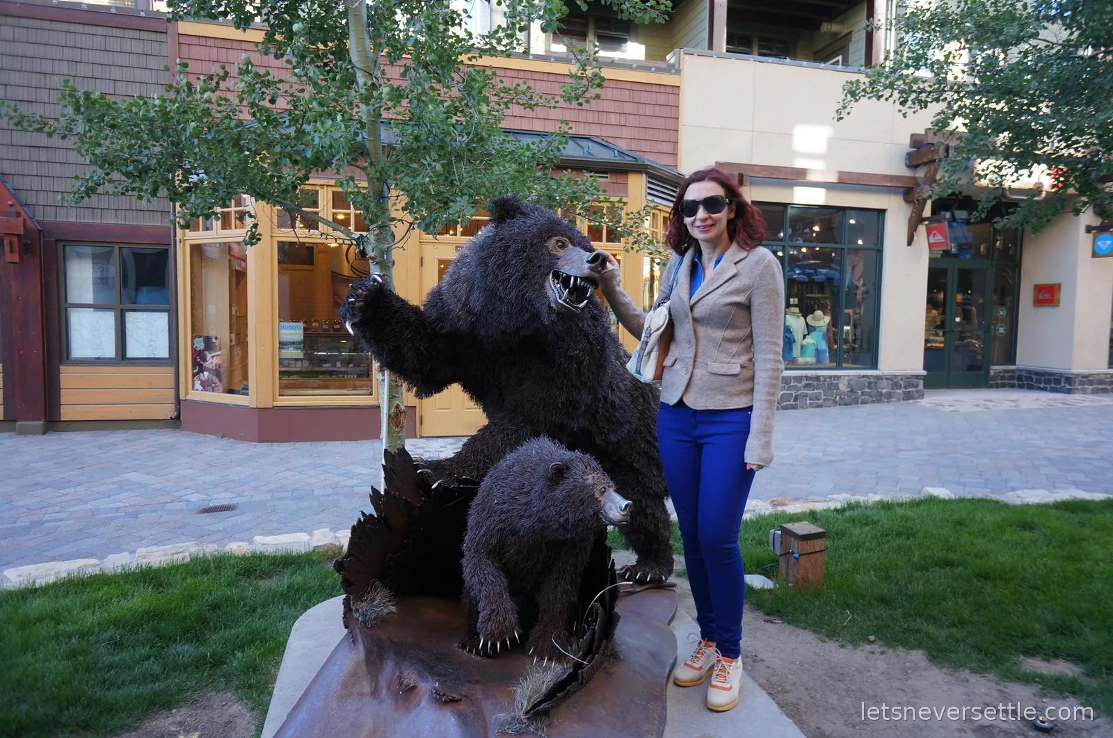 Inga standing with a carved bear statue rearing beside a tree in the village square, a cub at its feet