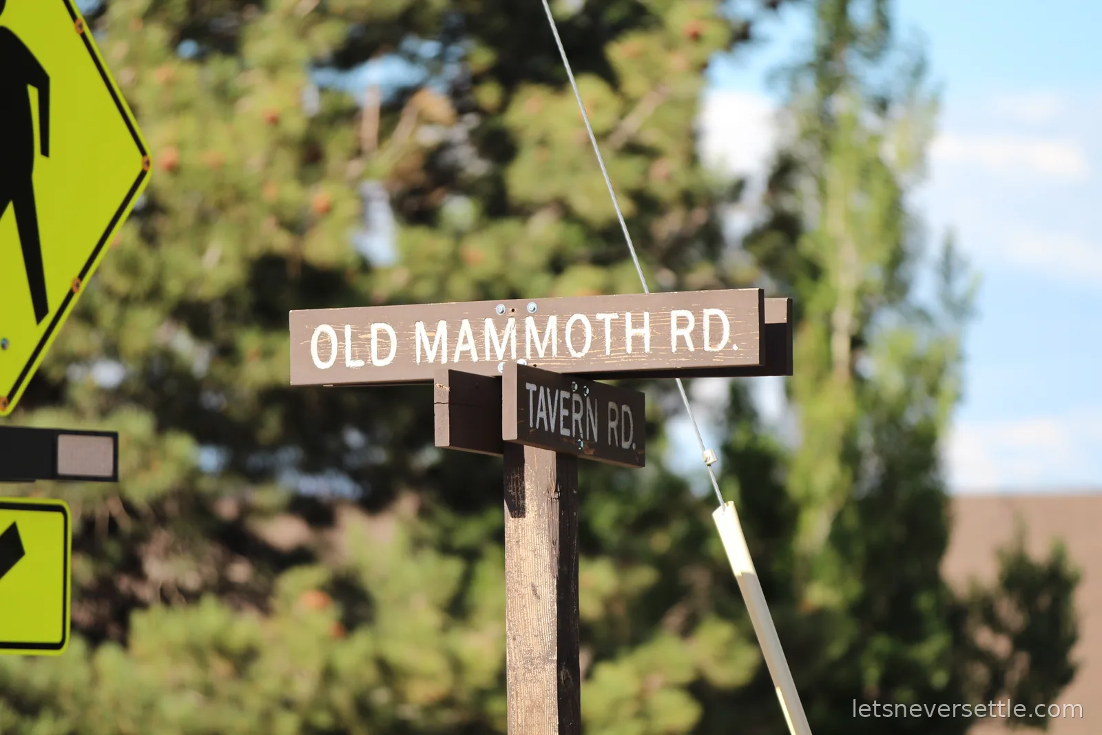 Wooden street signs reading Old Mammoth Road and Tavern Road against pine trees