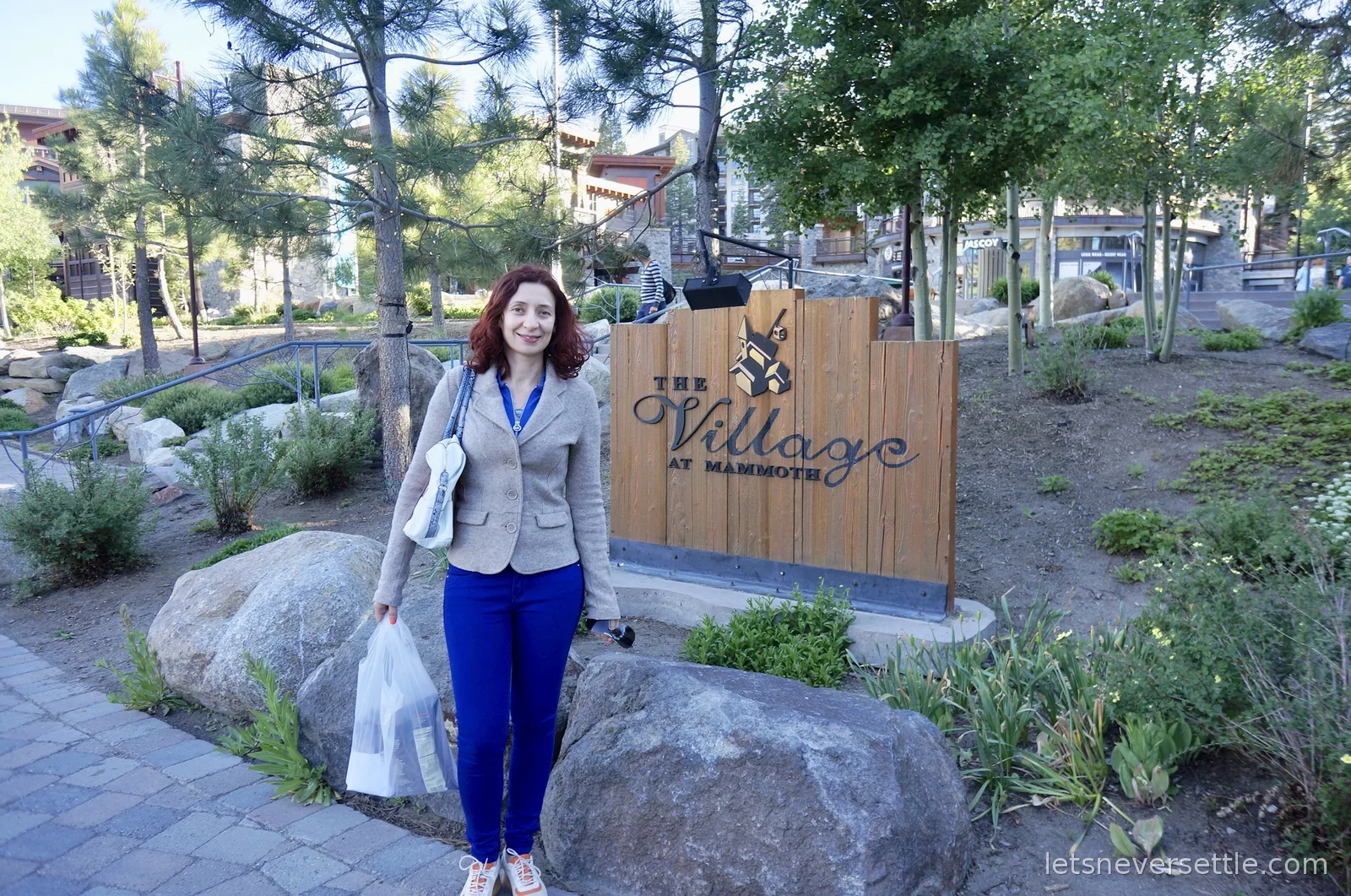 Inga beside the wooden Village at Mammoth sign set among boulders, pines and aspens