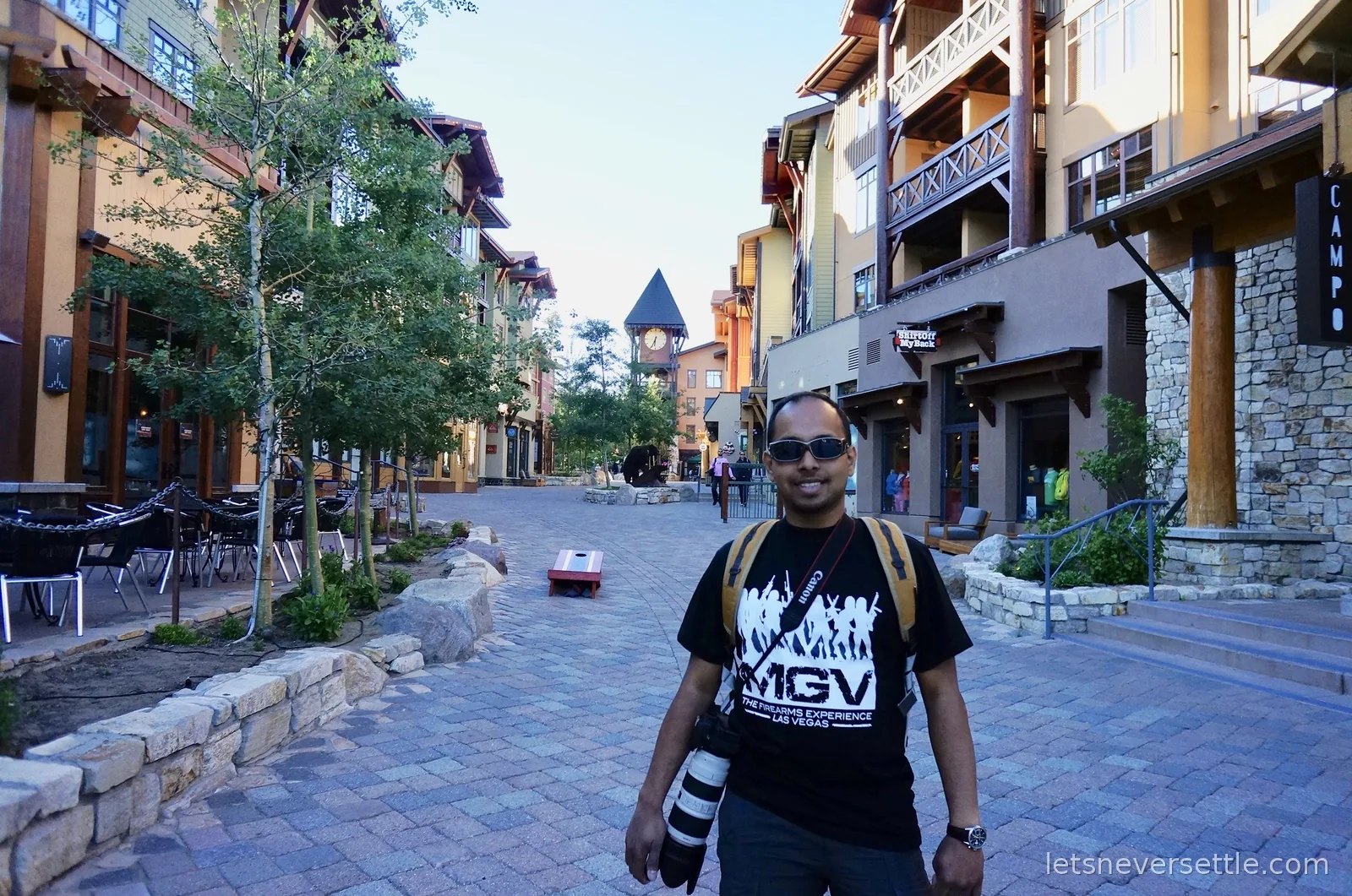 Dileep on the quiet paved lane of the Mammoth village with timber lodges, empty cafe tables and a clock tower behind