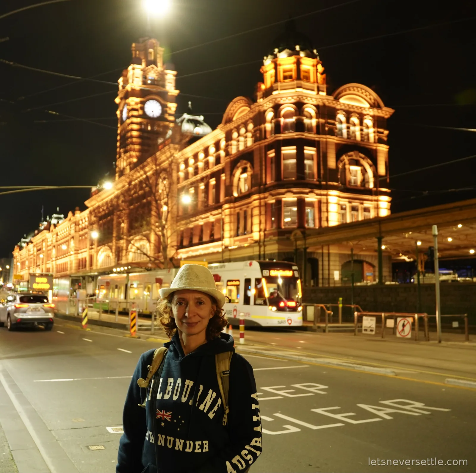 Inga in front of the illuminated Flinders Street Station at night with its clock tower and dome, a tram passing behind