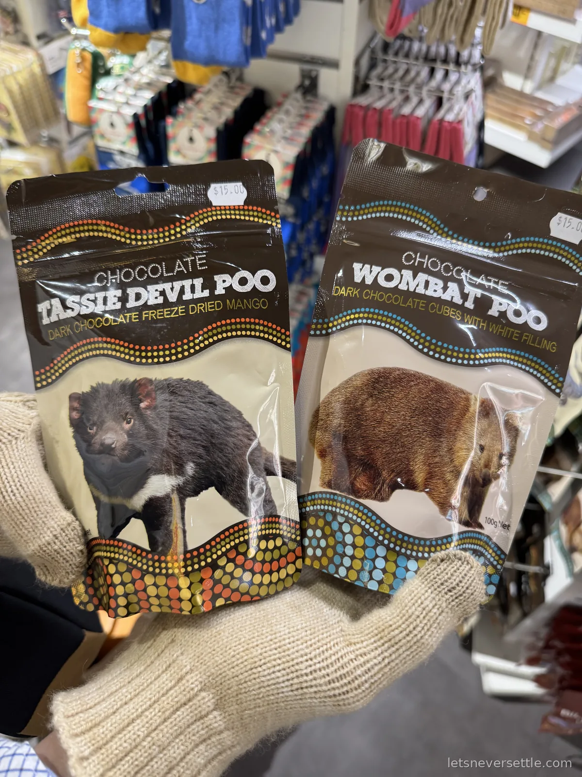 Gloved hands holding bags of Chocolate Tassie Devil Poo and Chocolate Wombat Poo in a souvenir shop, priced 15 dollars