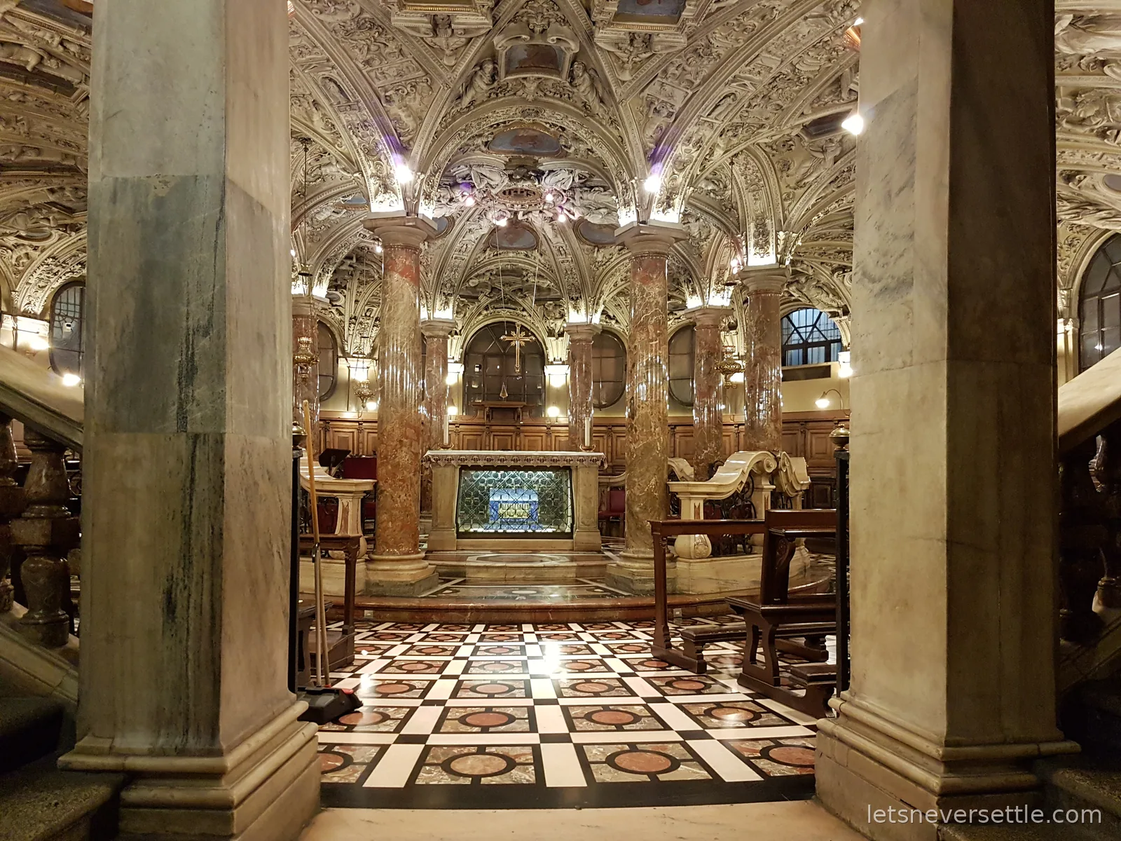 An ornate underground chapel with marble columns, a carved plaster ceiling and a chequered marble floor, lit warm gold
