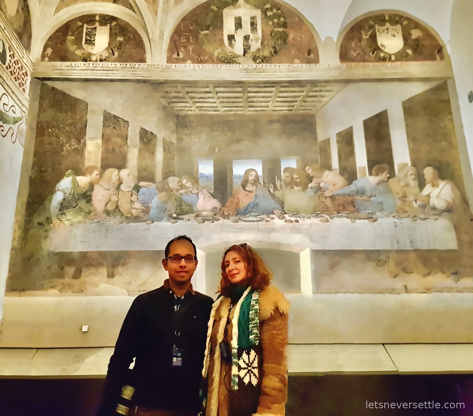 Inga and Dileep standing in the refectory below Leonardo's Last Supper mural, which covers the whole end wall above them