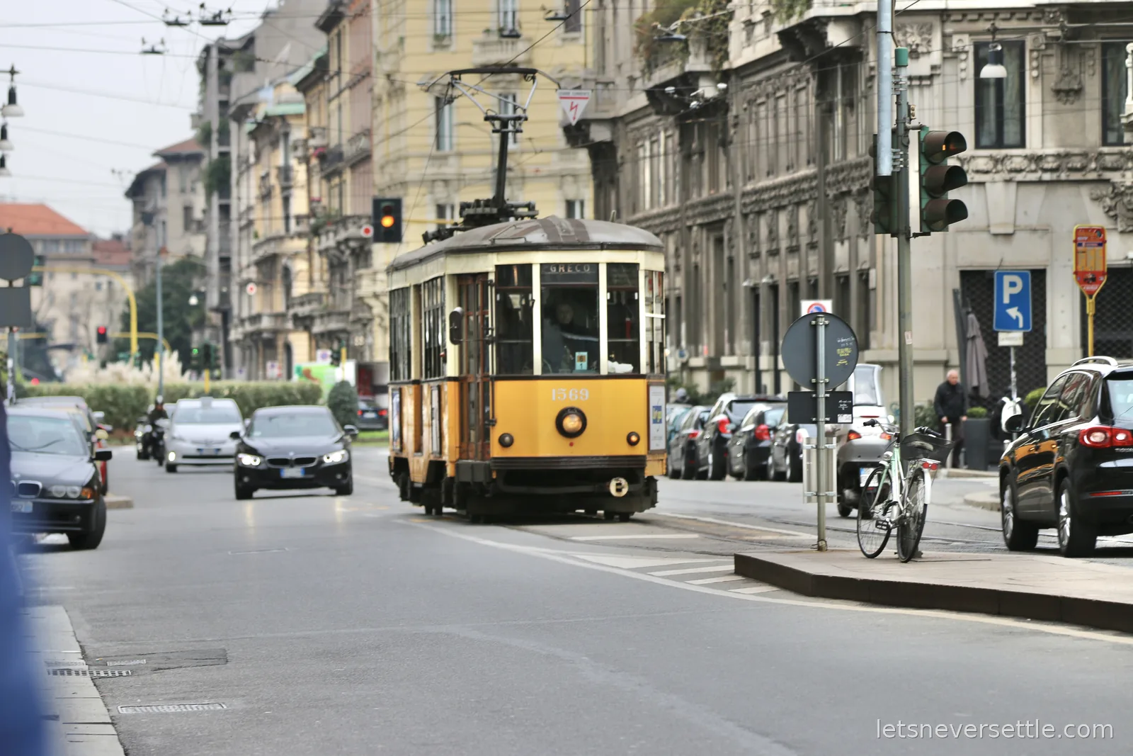 A vintage cream and orange Milan tram coming down a street lined with parked cars and tall apartment buildings