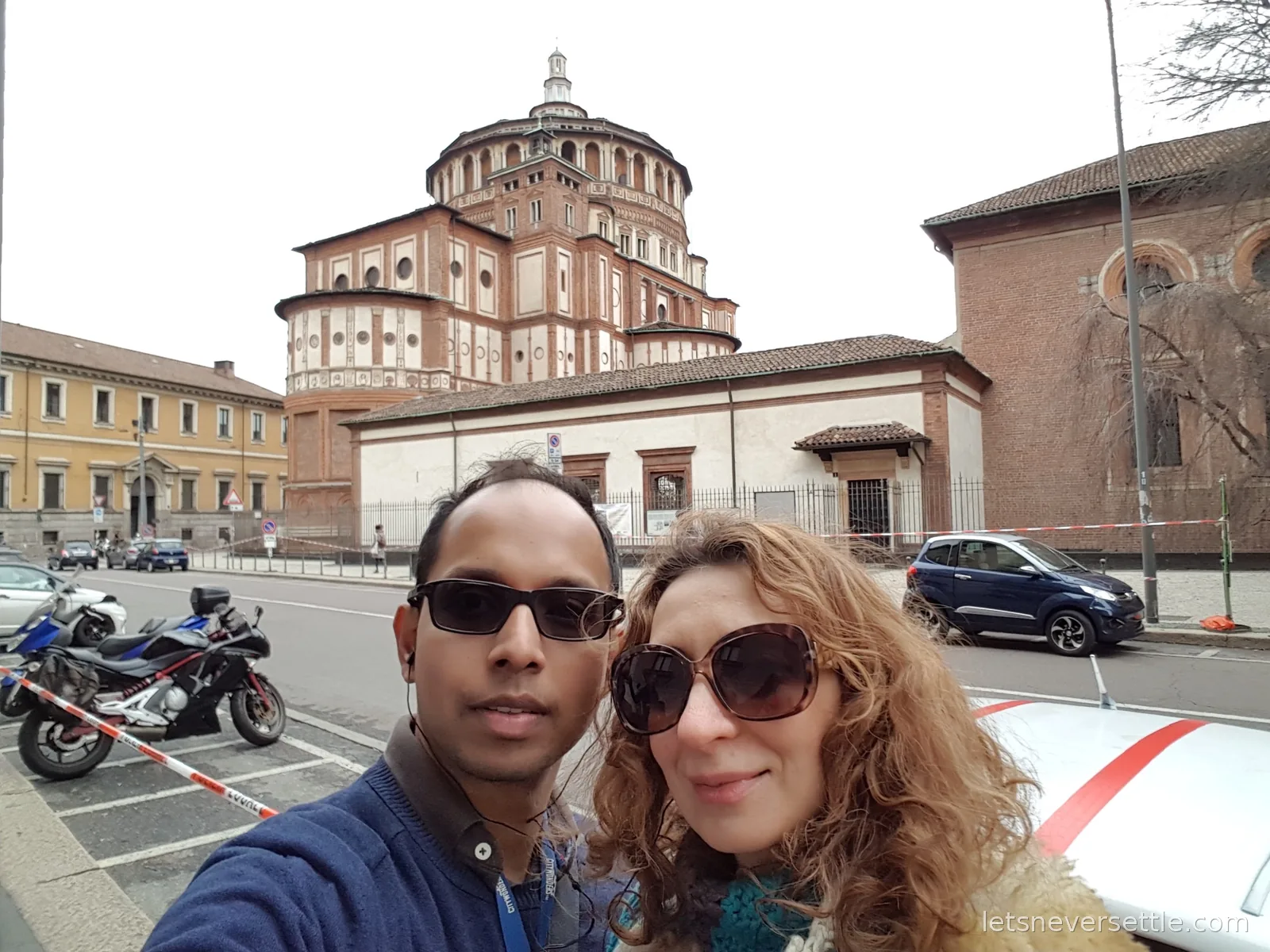 Inga and Dileep taking a selfie outside the brick apse and dome of Santa Maria delle Grazie church in Milan