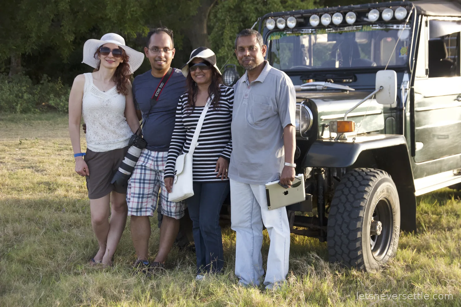Four travellers lined up in front of a dark green safari jeep with a row of spotlights above the windscreen at Minneriya