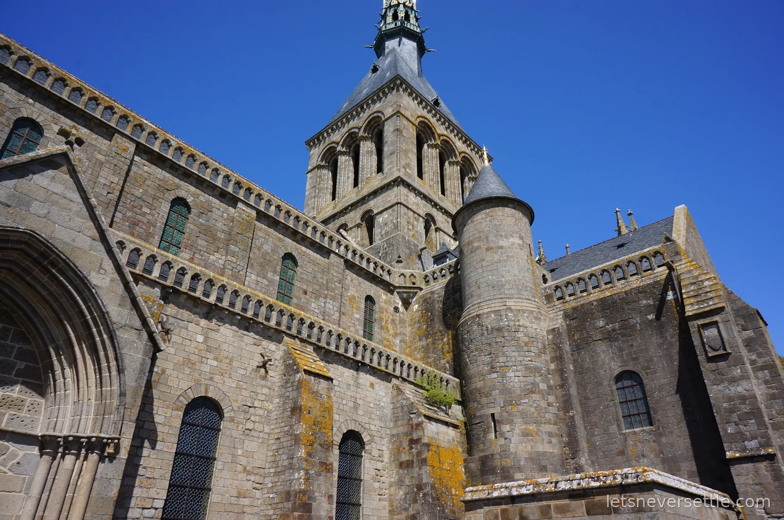 The abbey church tower and turret of Mont Saint-Michel against a deep blue sky
