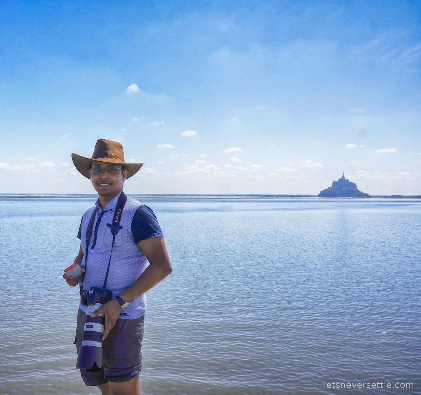 Dileep standing in the bay at low tide with Mont Saint-Michel small on the horizon behind him