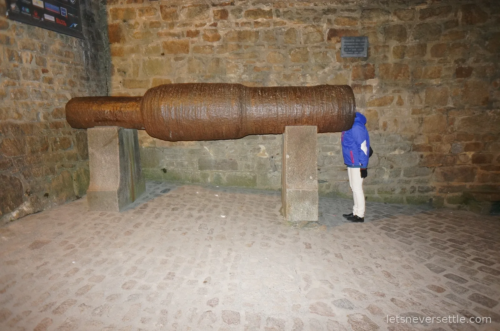 Inga peering into the barrel of a huge medieval cannon by the entrance of Mont Saint-Michel