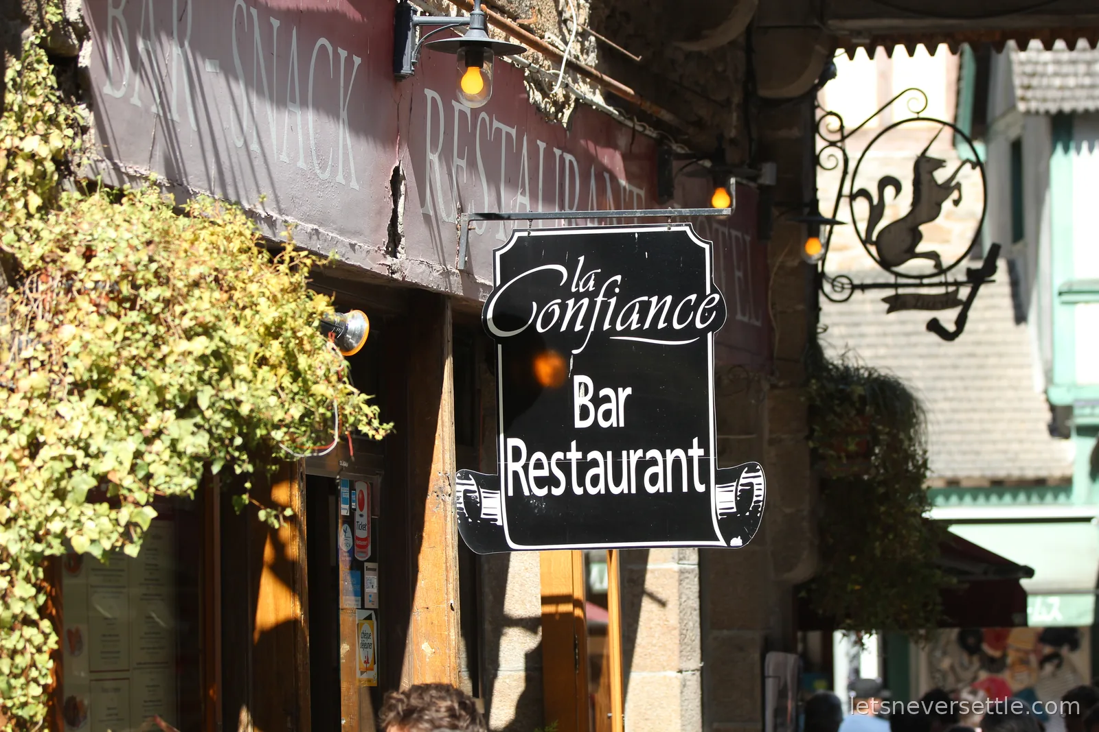 The hanging sign of La Confiance bar restaurant on the narrow main street of Mont Saint-Michel
