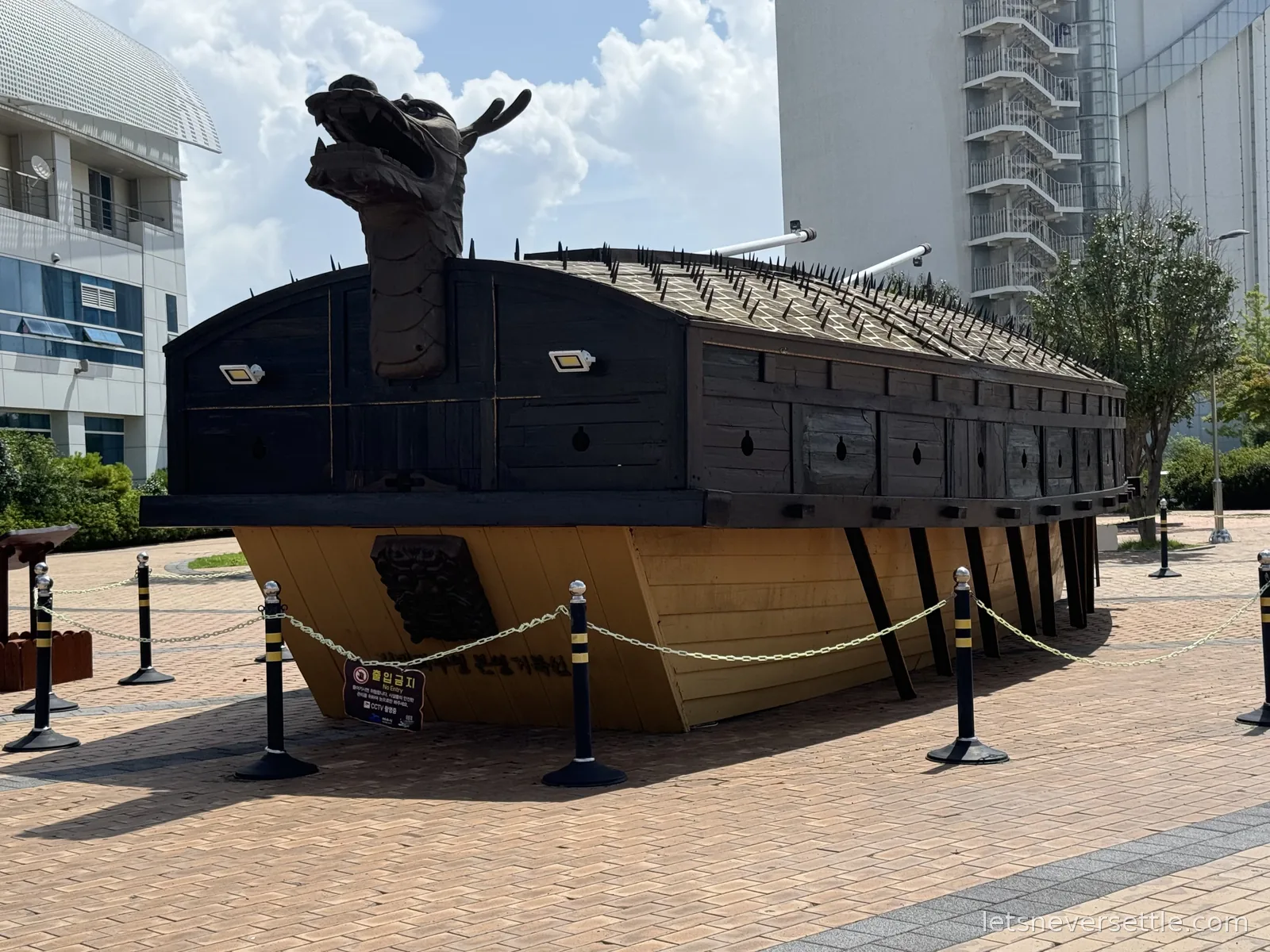 Full-size replica of a Korean turtle ship with a dragon figurehead and spiked wooden roof, displayed on a plaza