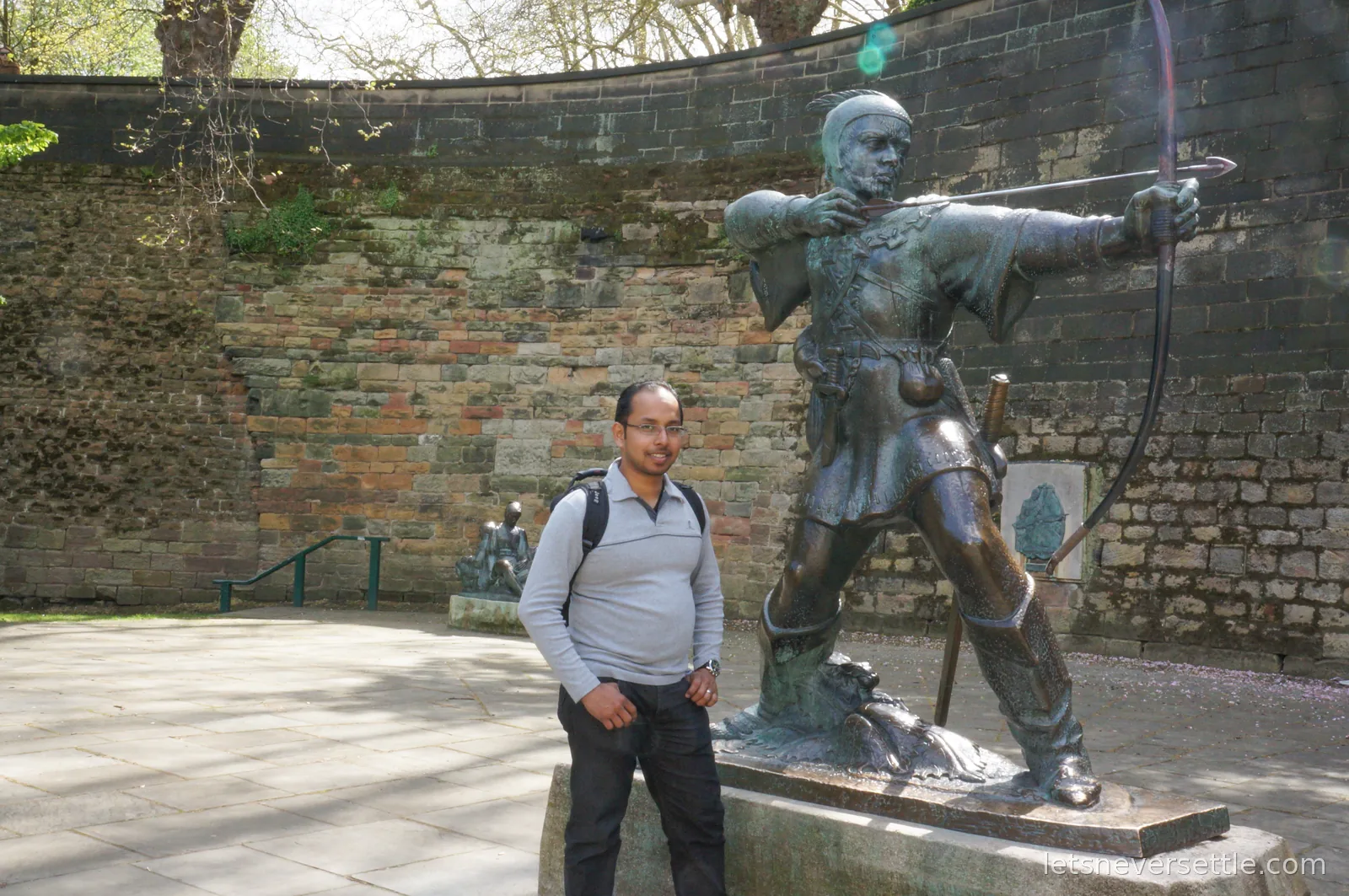Dileep in a grey jumper posing beside the bronze Robin Hood statue aiming his arrow along the wall of Nottingham Castle