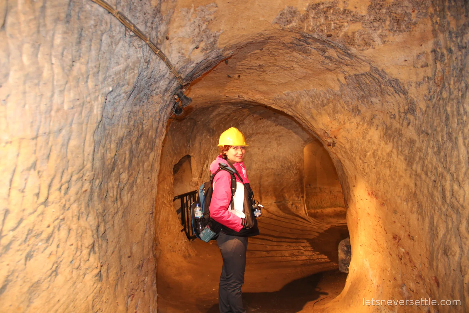 Inga in a yellow hard hat standing in a smooth arched tunnel carved through orange sandstone beneath Nottingham