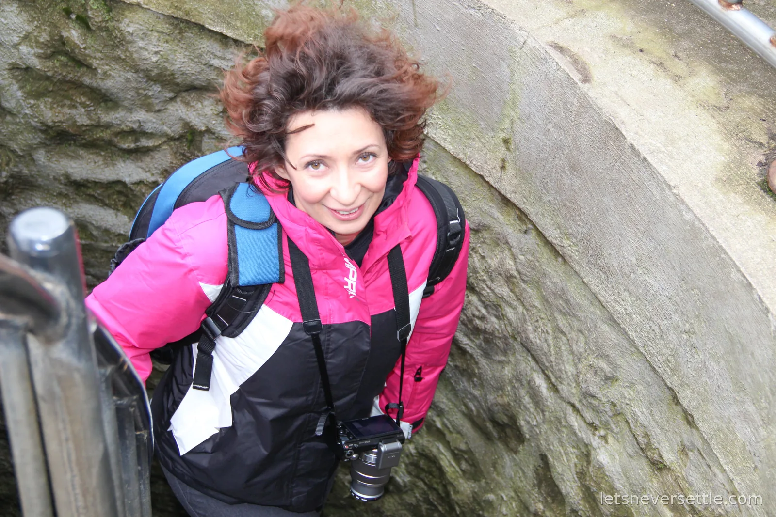 Inga with a camera around her neck looking up from a narrow stone spiral staircase with a metal handrail