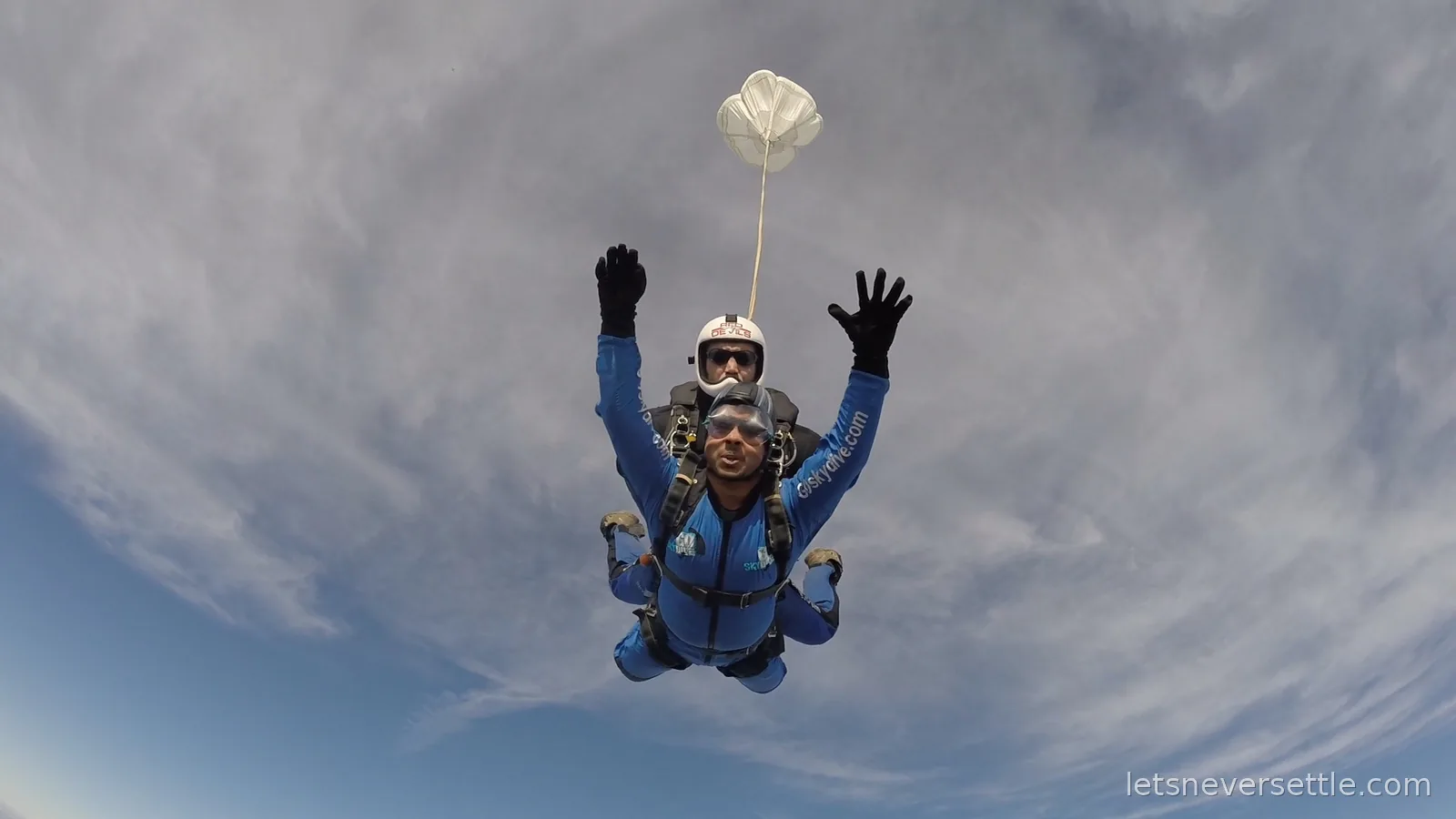 Dileep and his tandem instructor in freefall with hands spread wide, the white drogue chute deployed above them