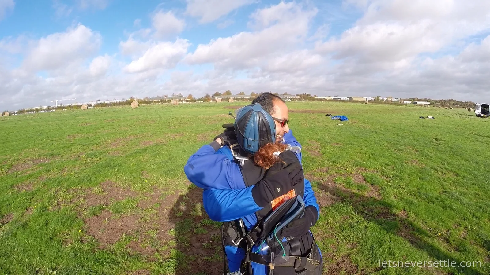 Inga and Dileep hugging on the airfield grass, still wearing helmets and harnesses
