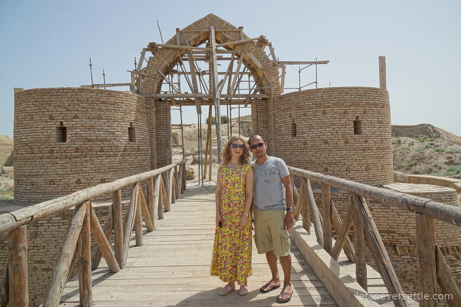 Inga and Dileep on a wooden bridge in front of the rebuilt brick entrance gate of Otrar, its arched portal held up by timber scaffolding