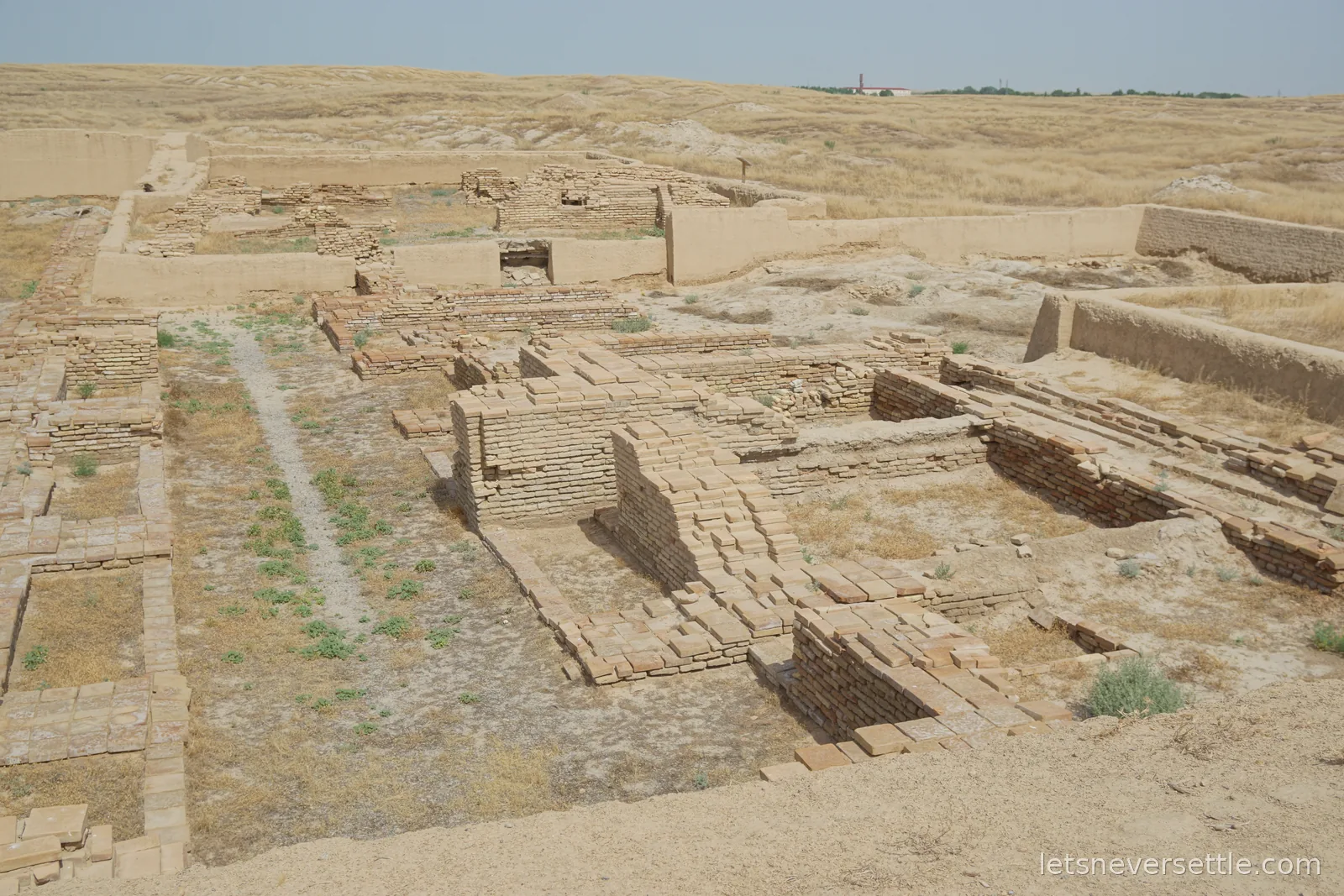 Excavated mud-brick walls and paved floors of the ancient city of Otrar under a hazy sky, dry steppe grass stretching to the horizon
